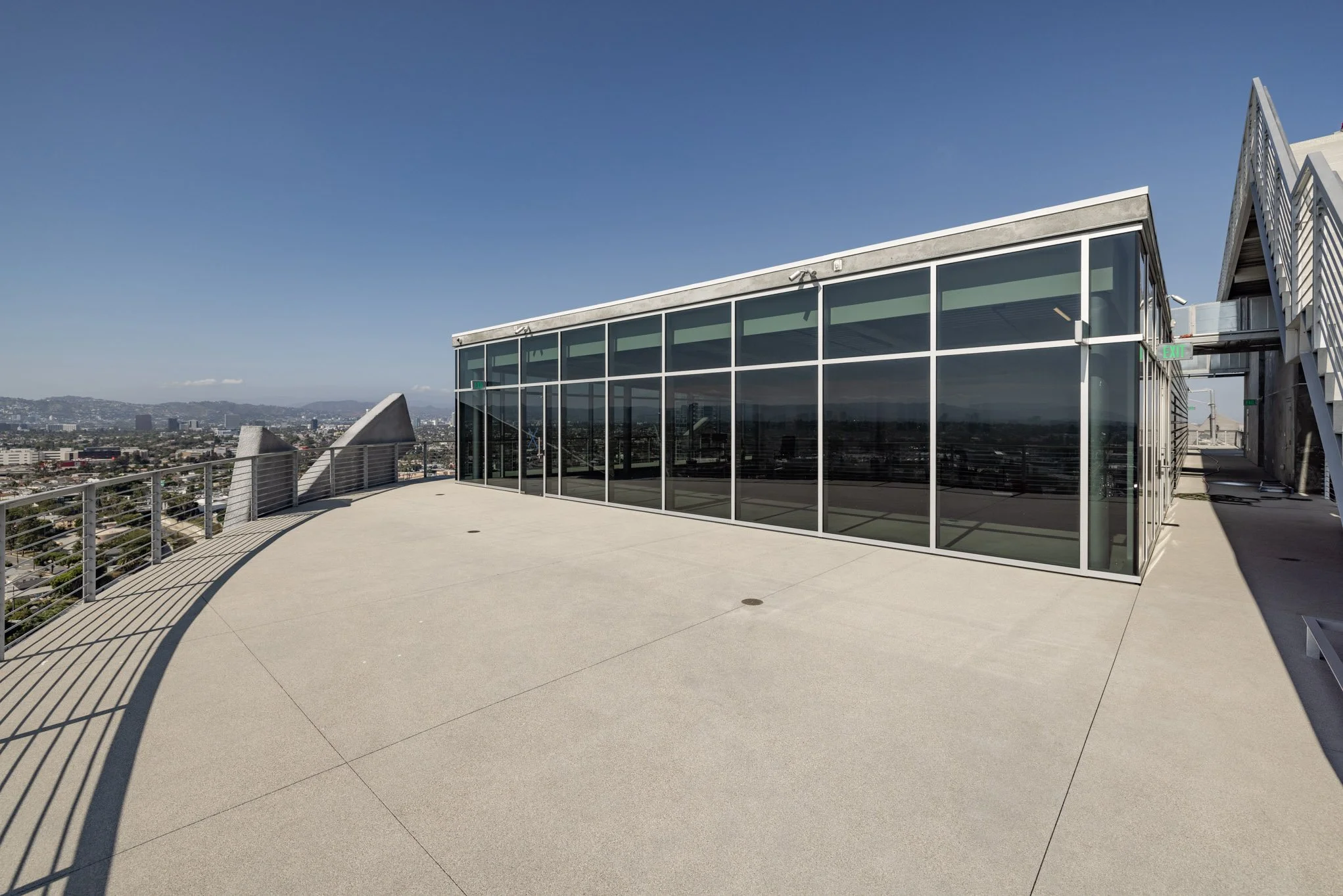 Empty rooftop terrace with glass-walled structure and city skyline in the background.