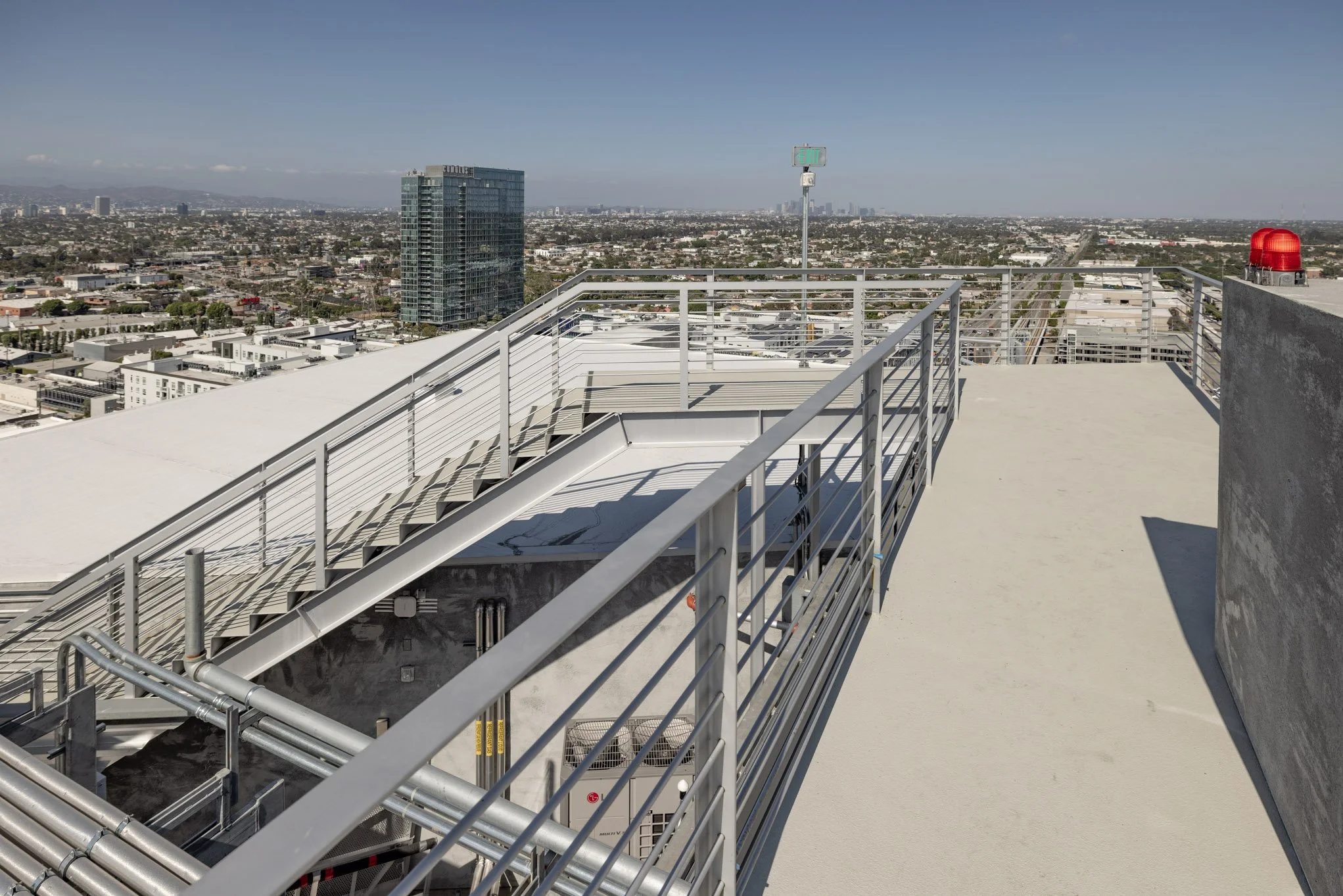 View from the rooftop of a tall building in Los Angeles showing cityscape with high-rise and low-rise buildings, a clear sky, and mountains in the background.
