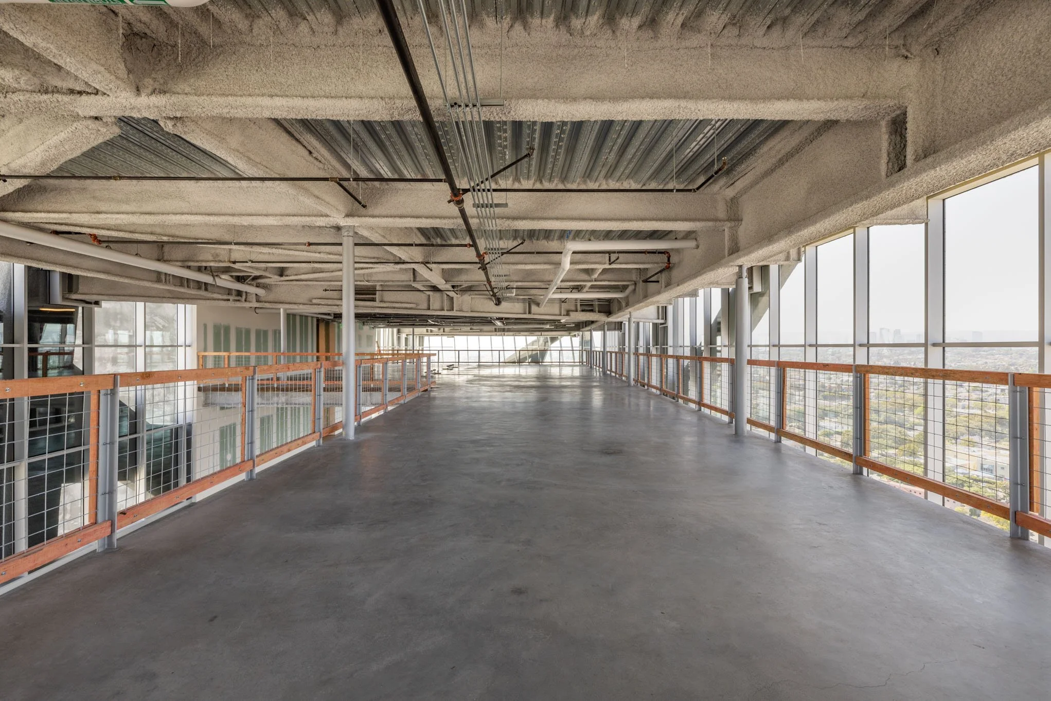 Empty construction floor in high-rise building with large windows and exposed ceiling pipes.