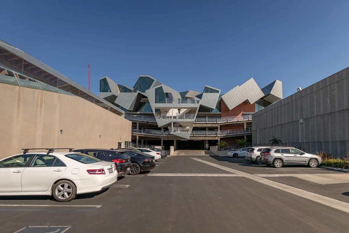 Modern building with geometric architectural design and a parking lot with several cars in the foreground.