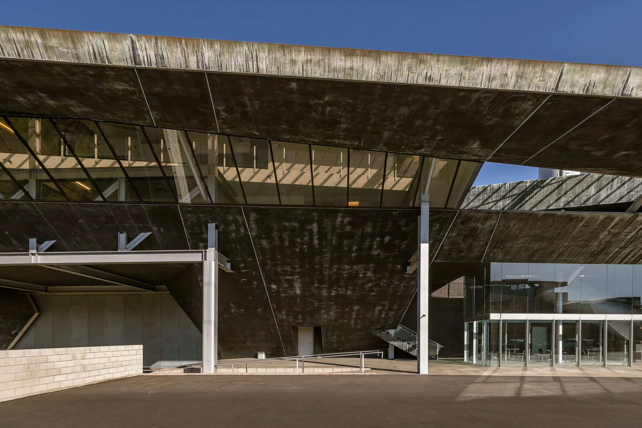 Modern multi-story building with black and glass exterior, featuring geometric shapes and large open entrance, under a clear blue sky.
