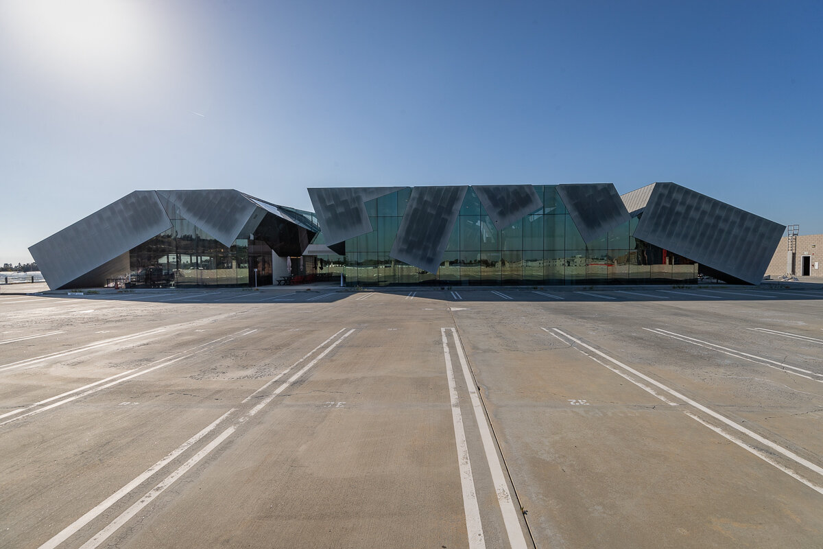 Modern building with angular metallic and glass exterior, set against a clear blue sky with an empty parking lot in front.
