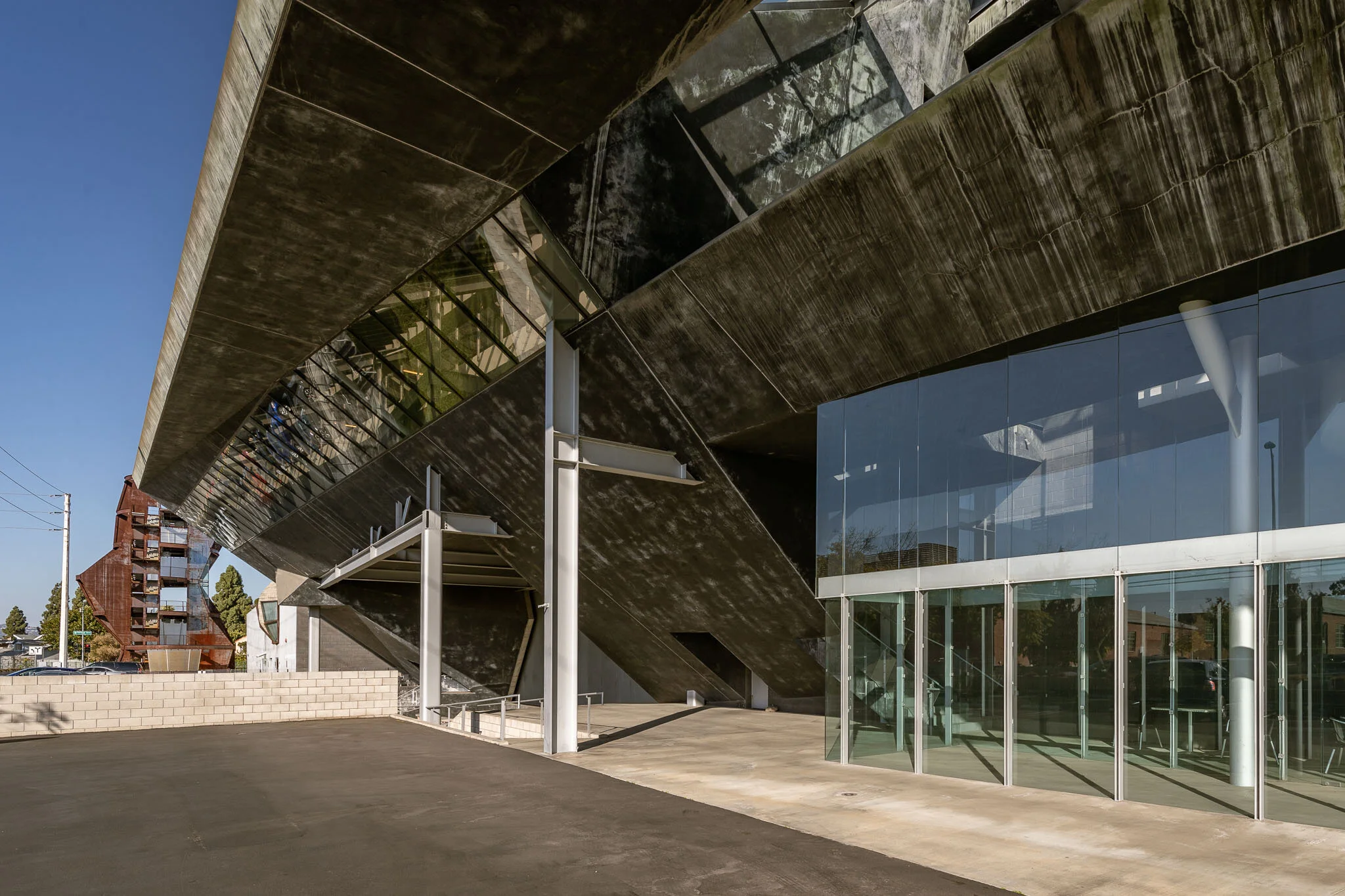 Modern architectural building with large glass windows, angular dark exterior surfaces, and exposed structural supports outside, under a clear blue sky.