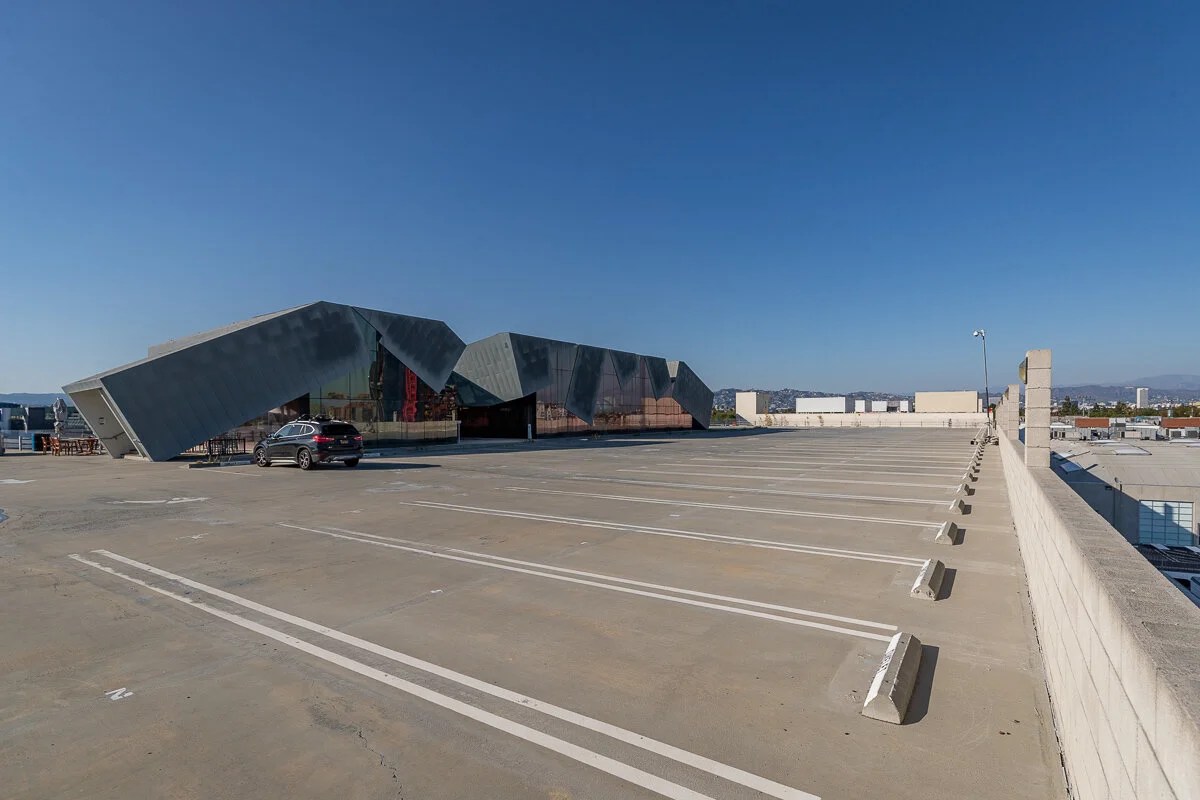 Rooftop parking lot with a modern angular black building and a few parked cars, under a clear blue sky.