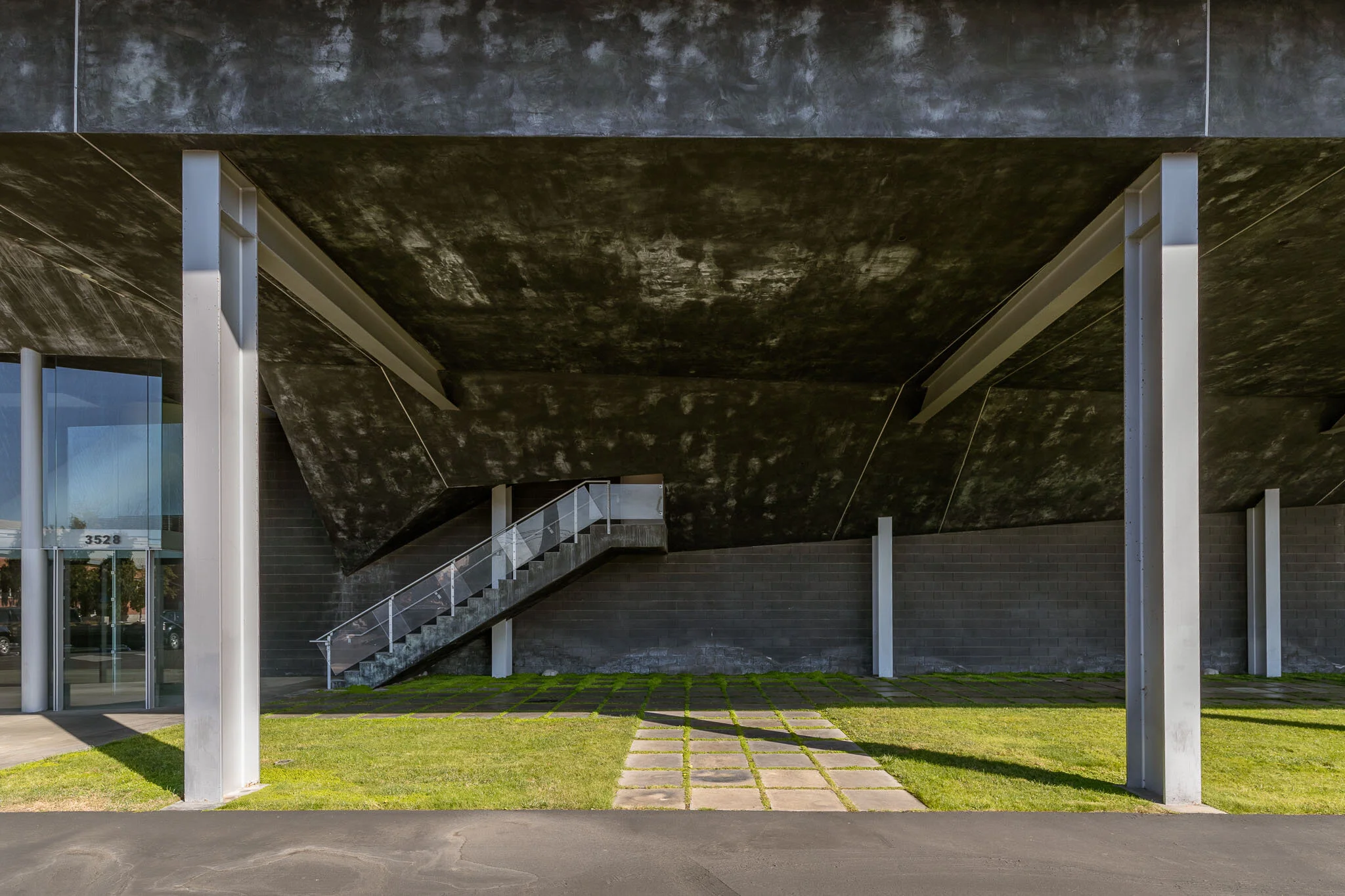 Modern building with black concrete exterior, glass doors, metal staircase, and a grassy area with stone pathway
