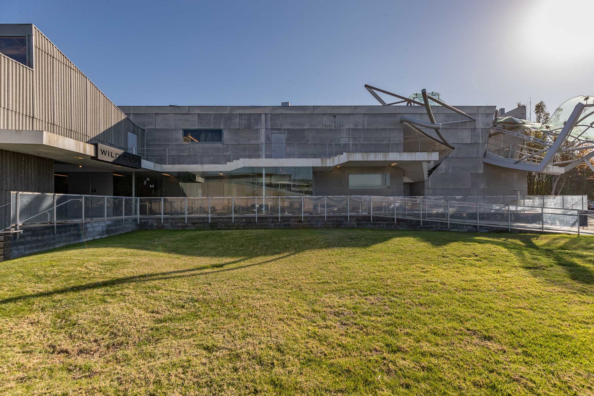 Exterior view of the Museum of Pop Culture, also known as MoPOP, in Seattle, featuring unique modern architecture with metallic and glass elements, a grassy foreground, and clear sky overhead.