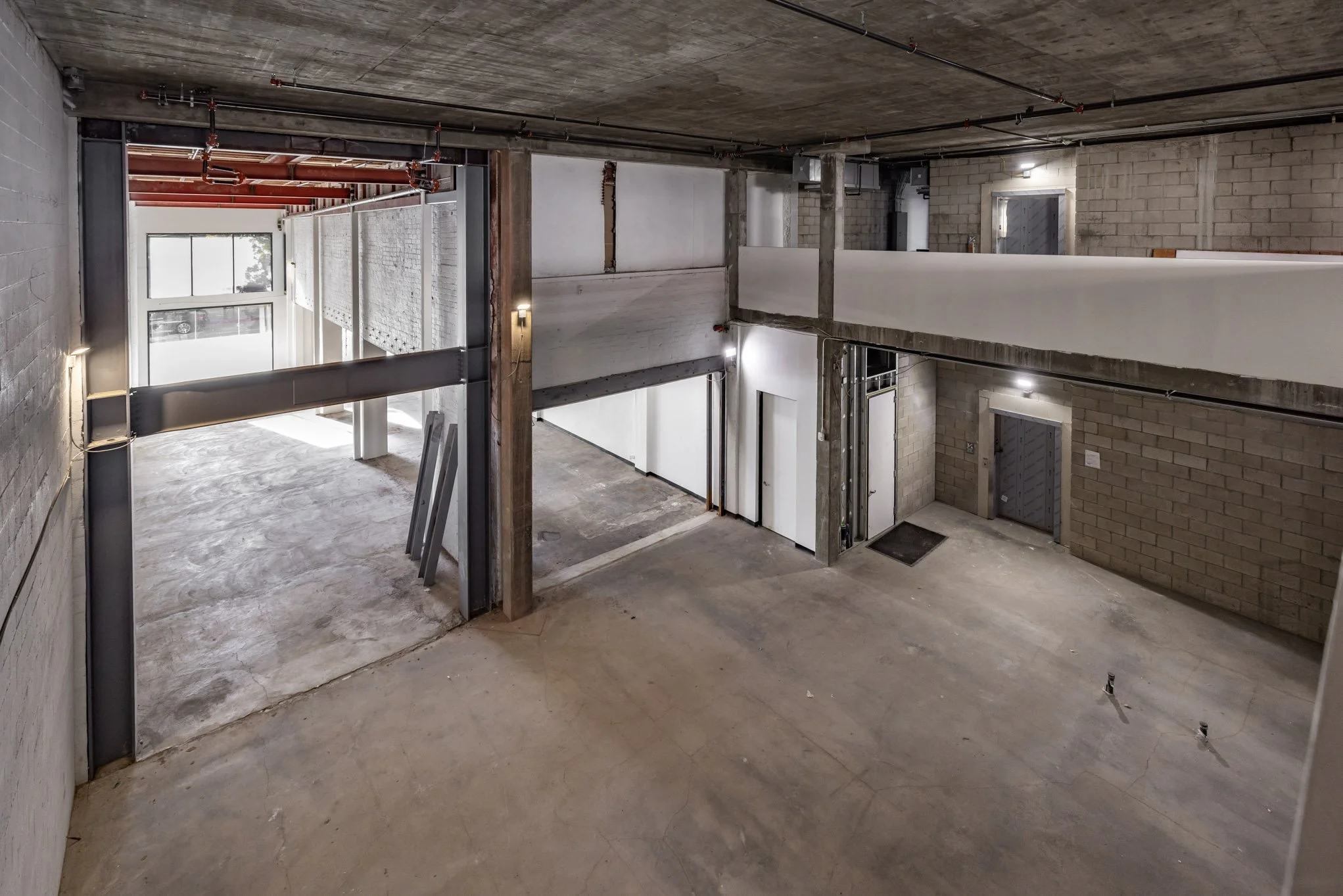 Interior of an unfinished multi-level commercial or industrial building with exposed concrete floors, concrete block walls, visible wiring and piping, and construction materials and equipment.