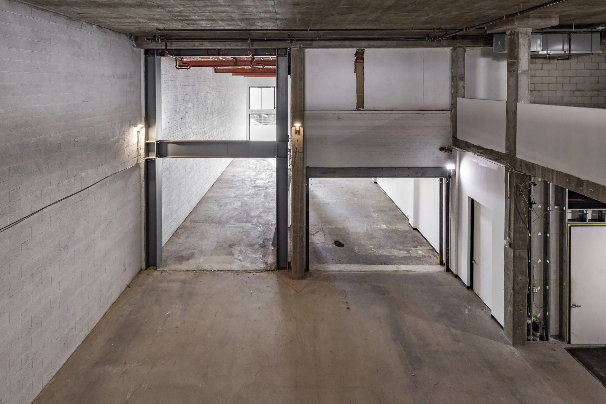 Empty indoor parking garage with concrete walls and floors, large steel beams, and an overhead sliding door.
