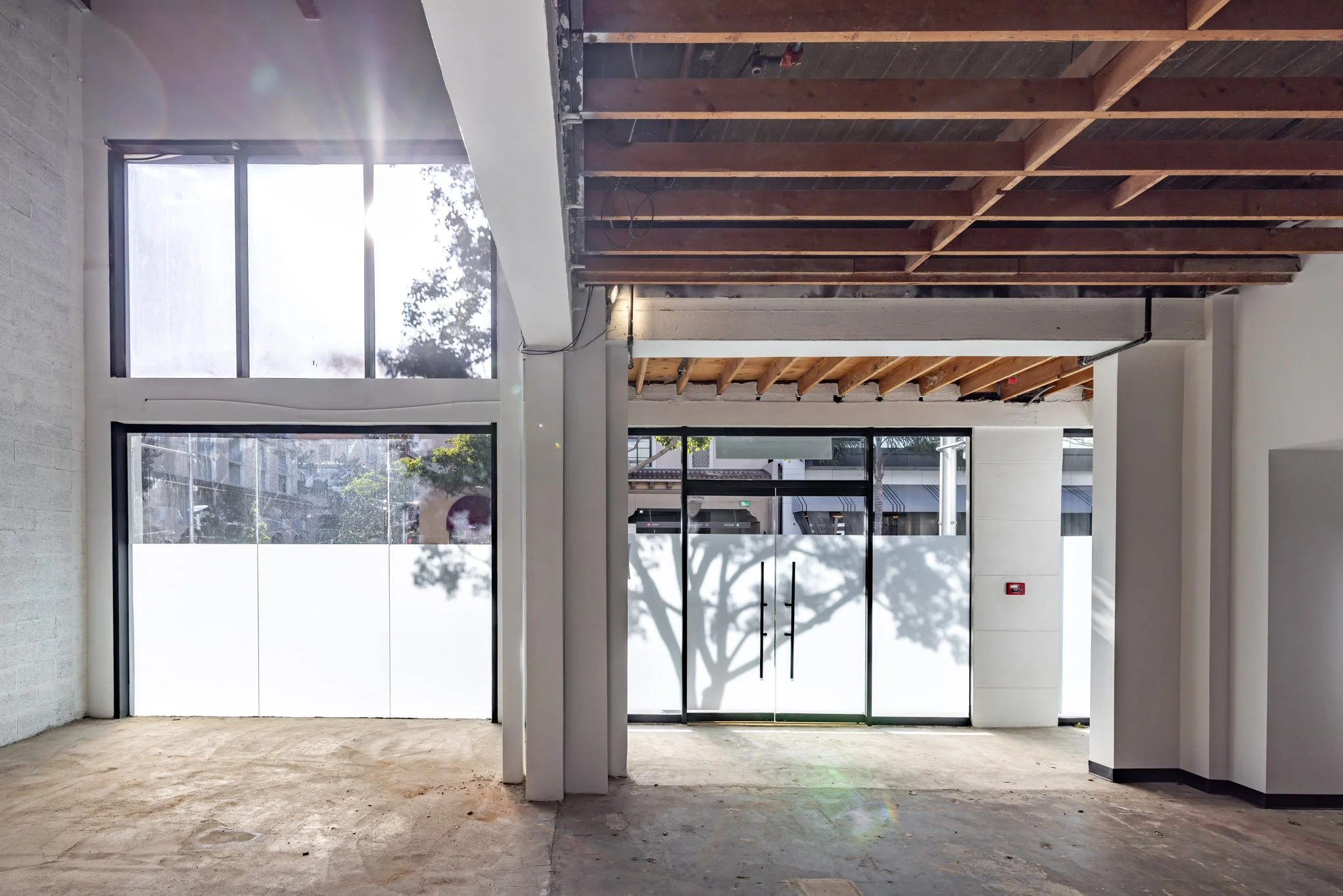 Interior of a building under construction with large windows, exposed ceiling beams, and a concrete floor.
