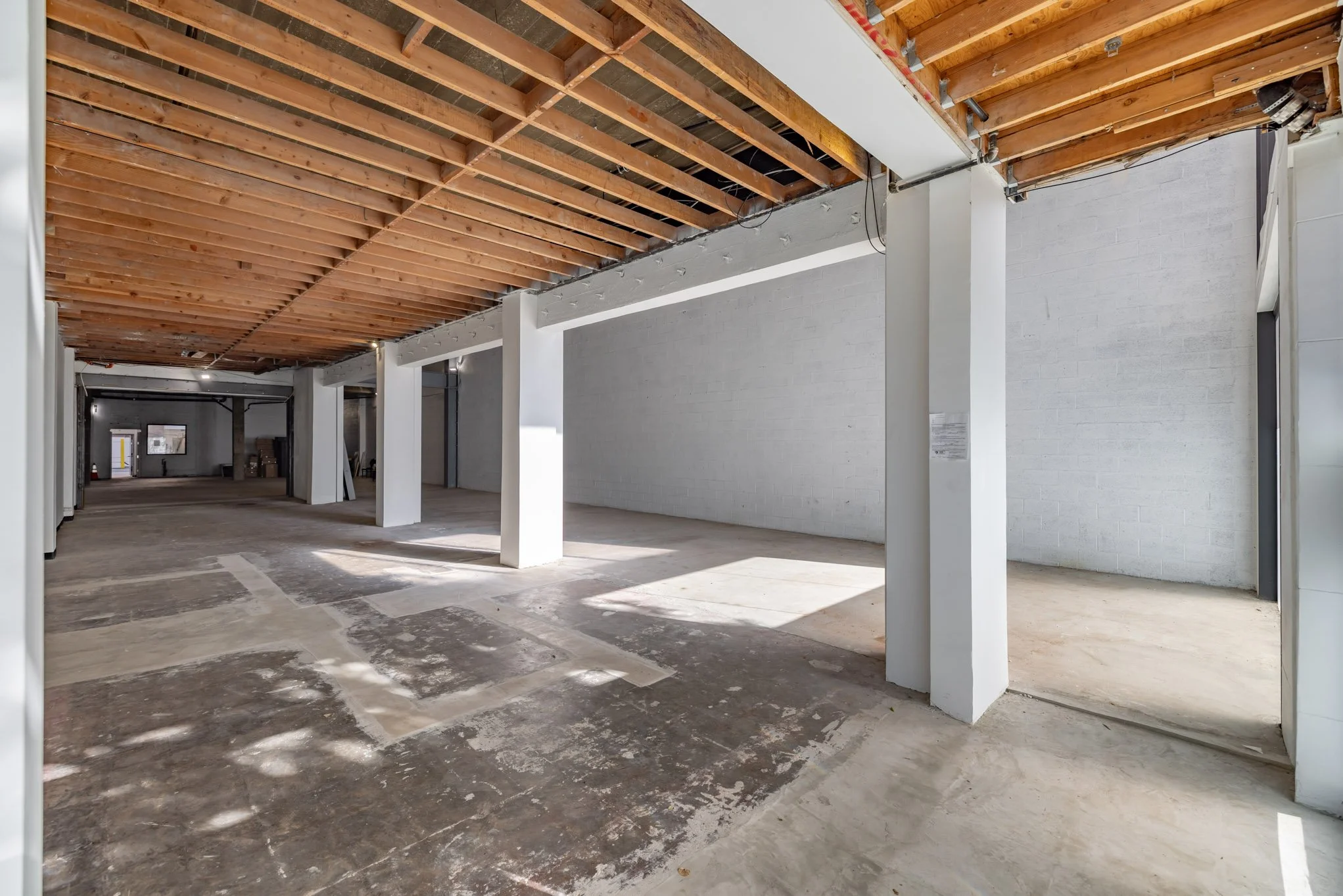 Empty commercial or industrial space with unfinished ceiling, white walls, and concrete floor.