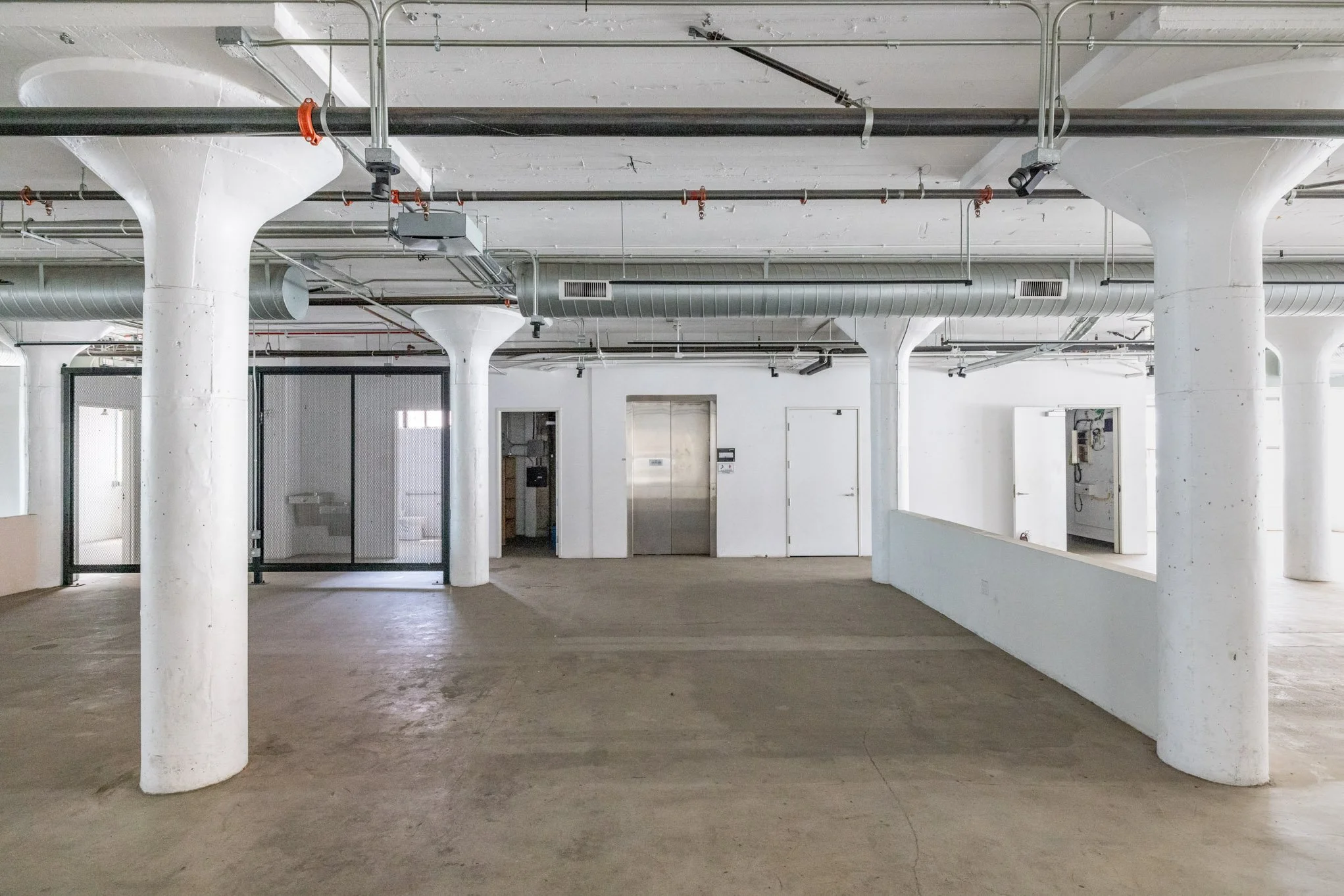 Empty underground parking garage with white supporting columns, concrete floor, and exposed ductwork on ceiling.