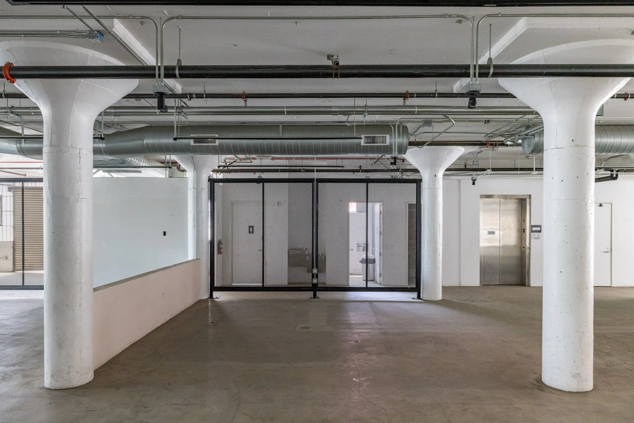 Empty indoor parking garage with white support columns, a glass door, and an elevator.