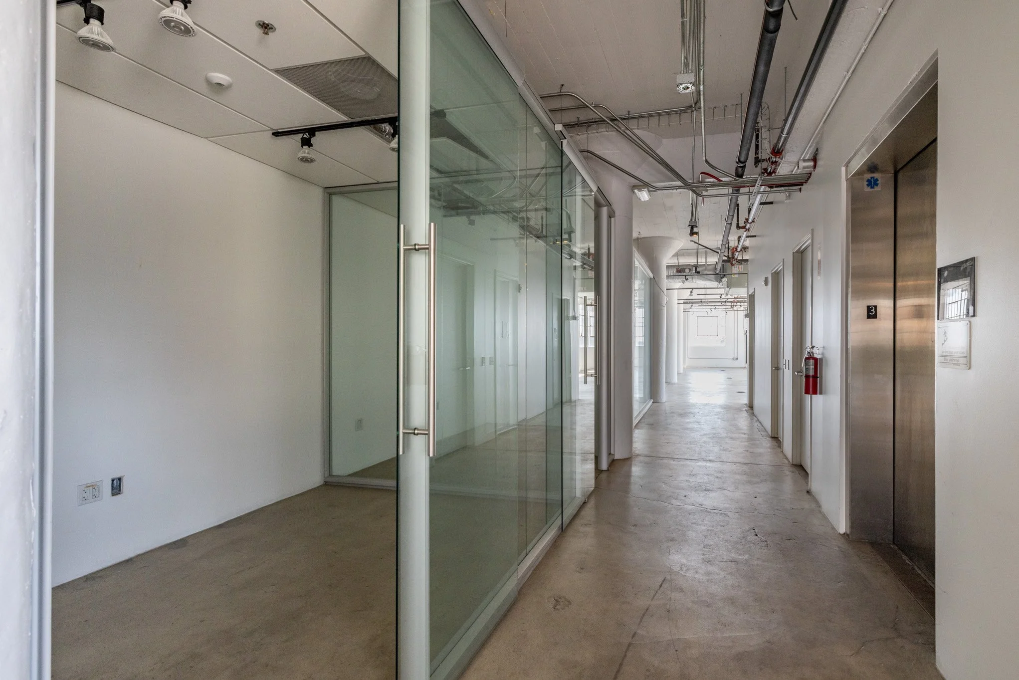 Empty corridor with glass office partitions and an elevator in a modern building