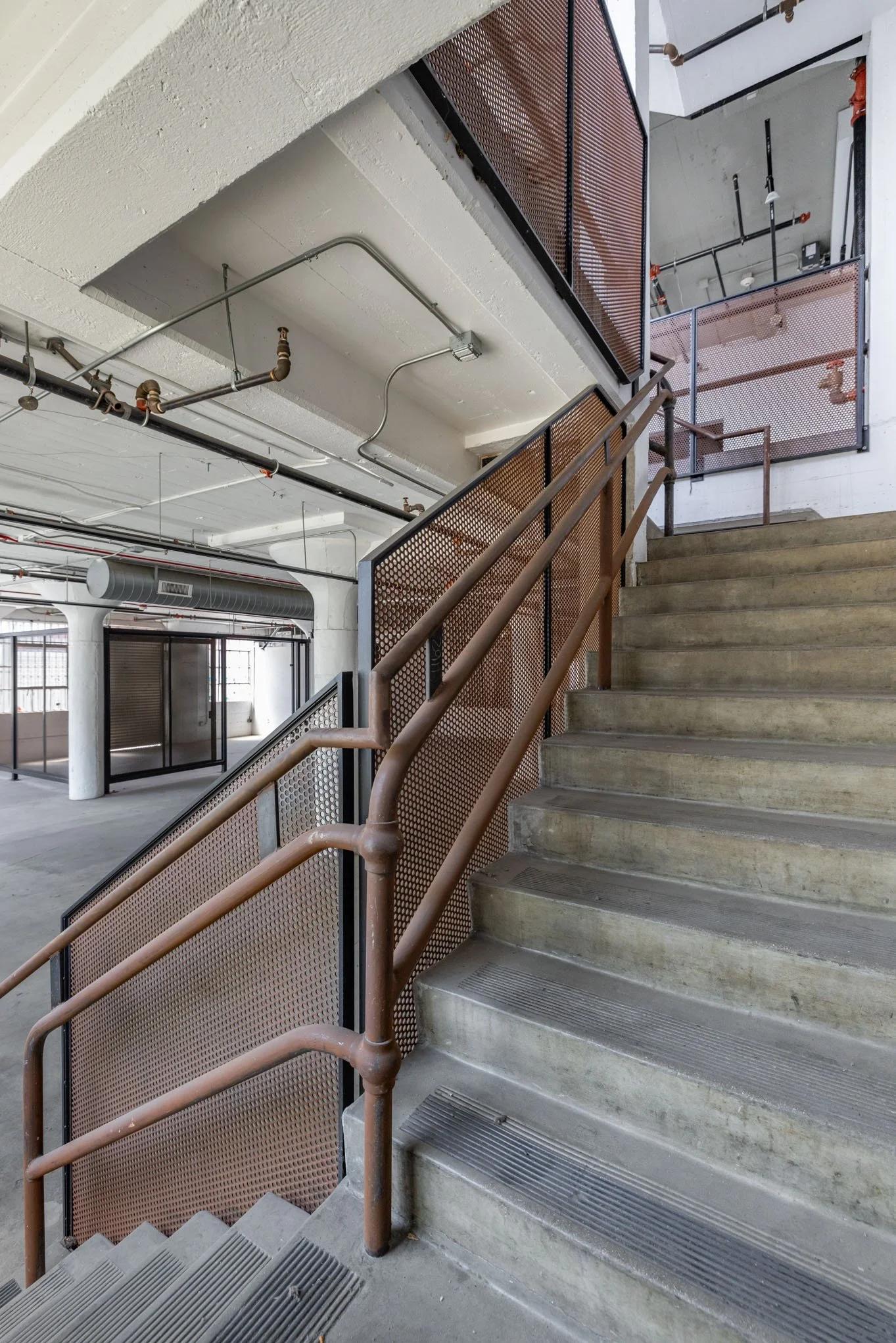 Concrete staircase with rust-colored metal handrails and perforated metal panels in an industrial-style building interior.