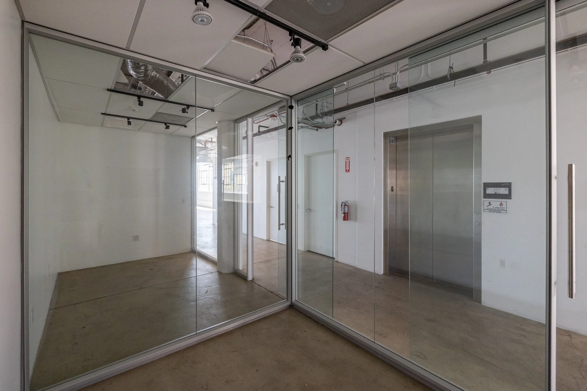 Empty commercial space with glass walls, elevator, and unfinished ceiling.