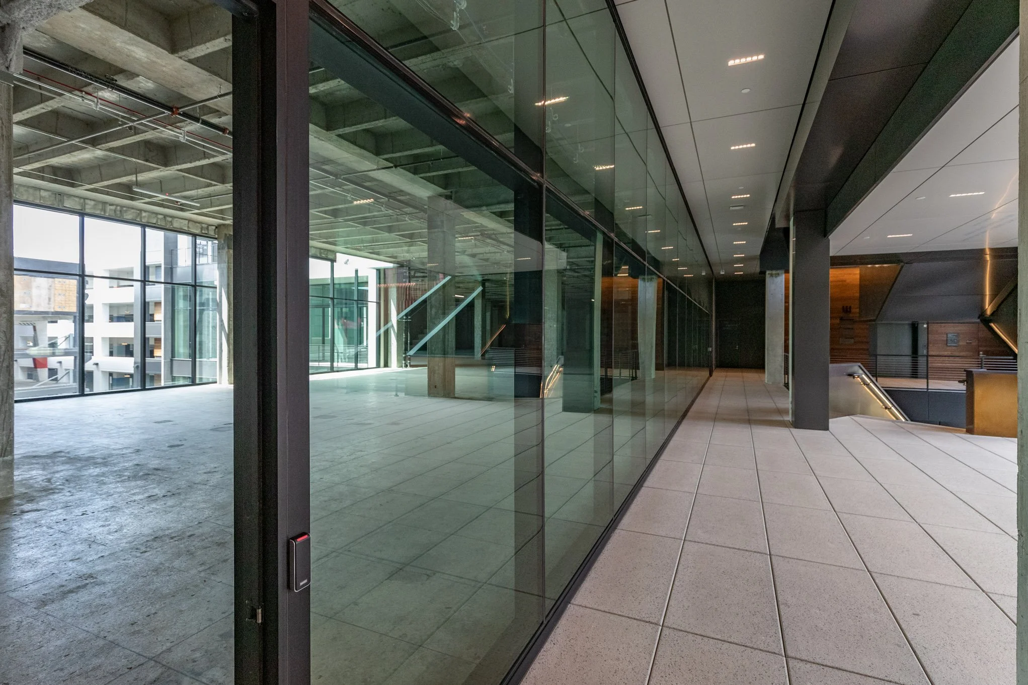Modern interior with glass walls, tiled flooring, staircases, and a balcony overlooking an urban cityscape.