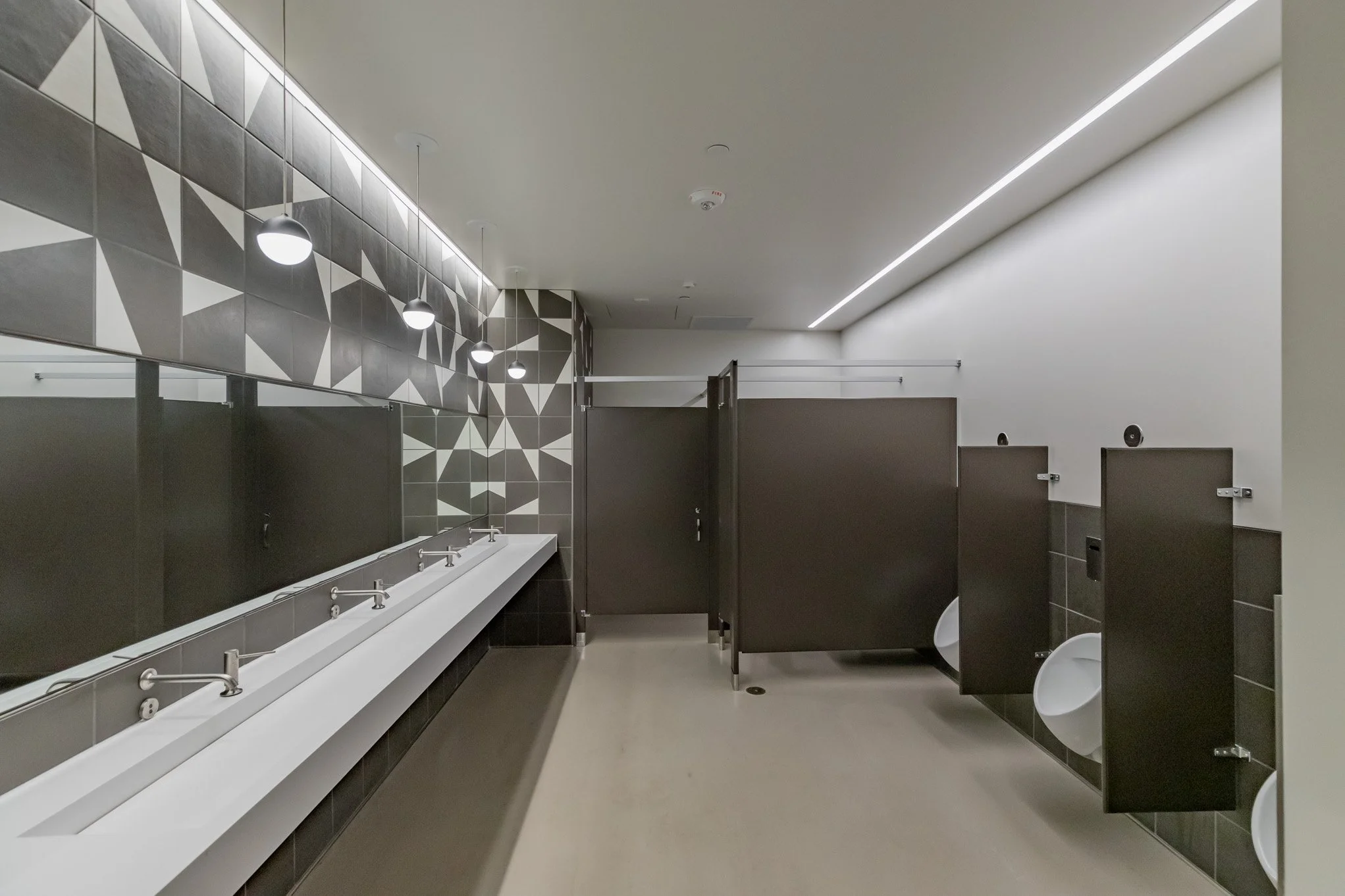 Empty men's and women's public restrooms with urinals, sinks, dark stall doors, and decorative wall tiles.