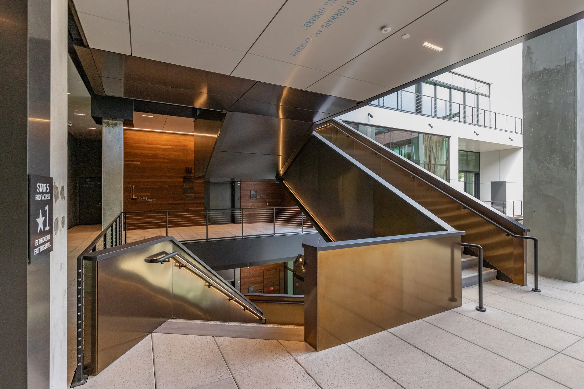Modern interior staircase with wooden and metal finishes, surrounded by glass and concrete walls, in a multi-story building.