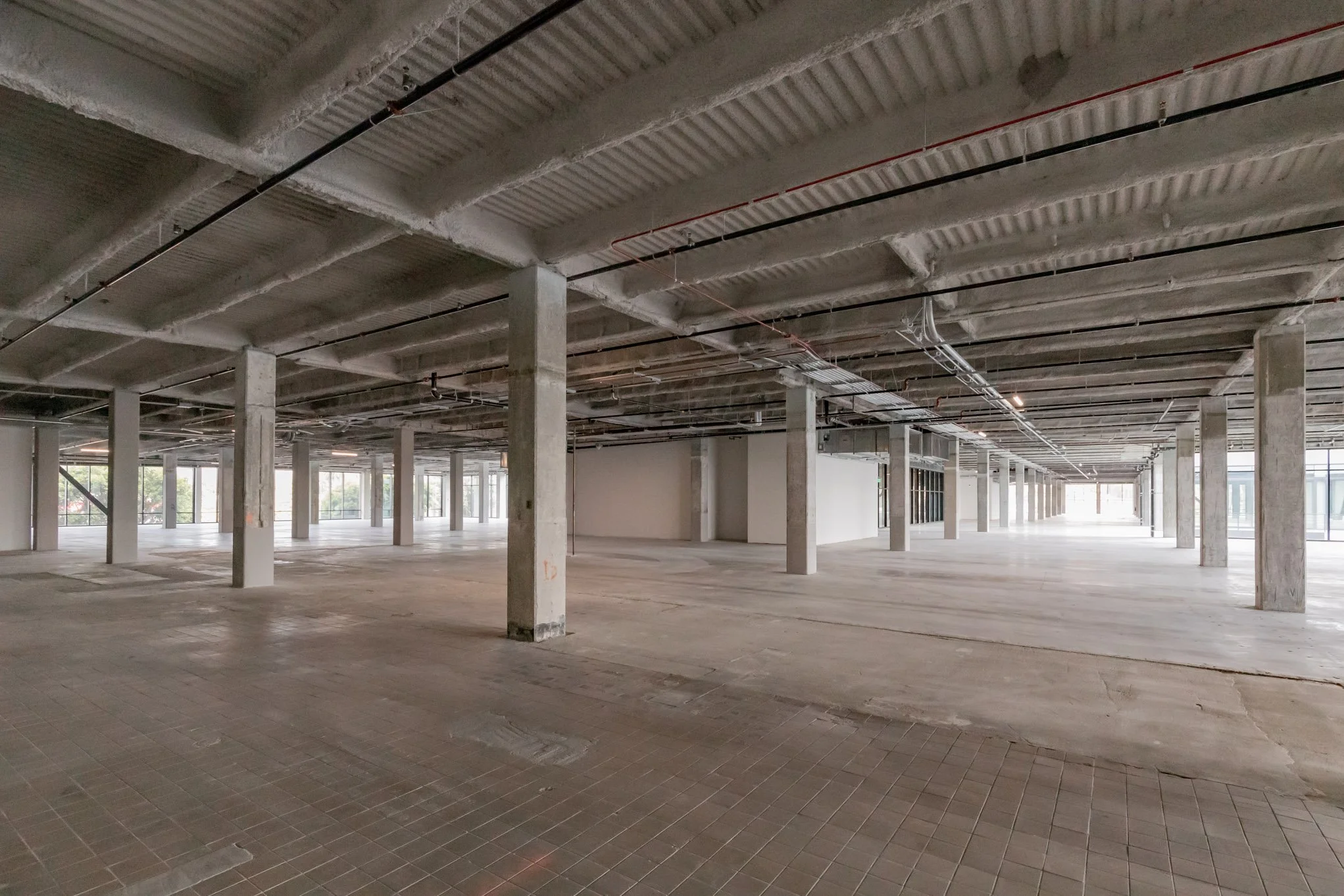 Empty commercial space with exposed ceiling, concrete columns, and large glass windows.