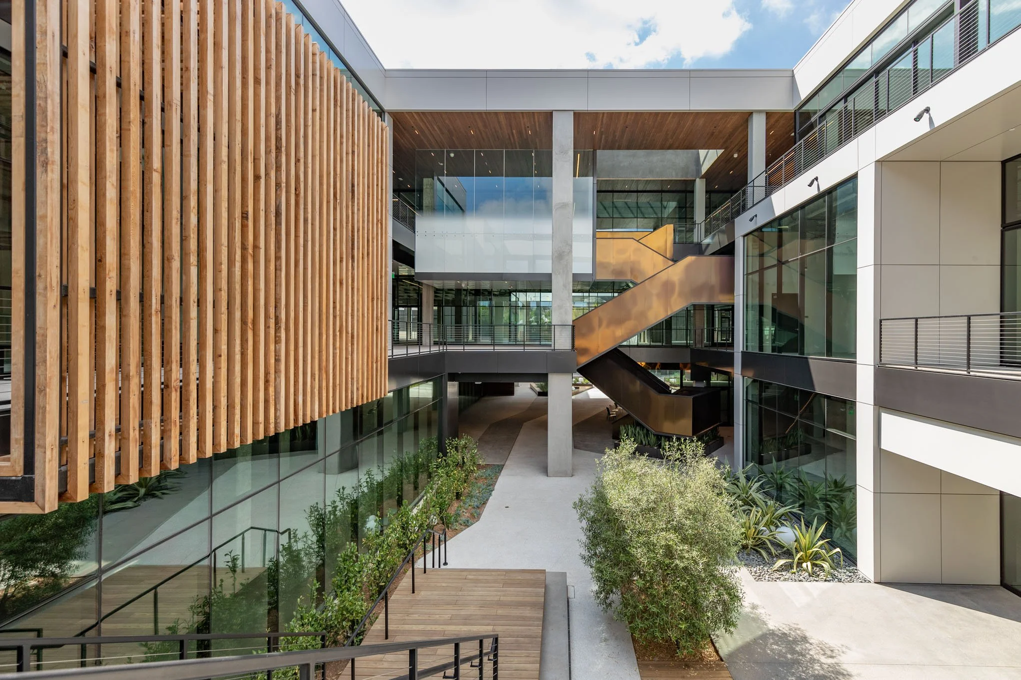 Modern building interior courtyard with glass walls, wooden accents, and a staircase with a copper finish.