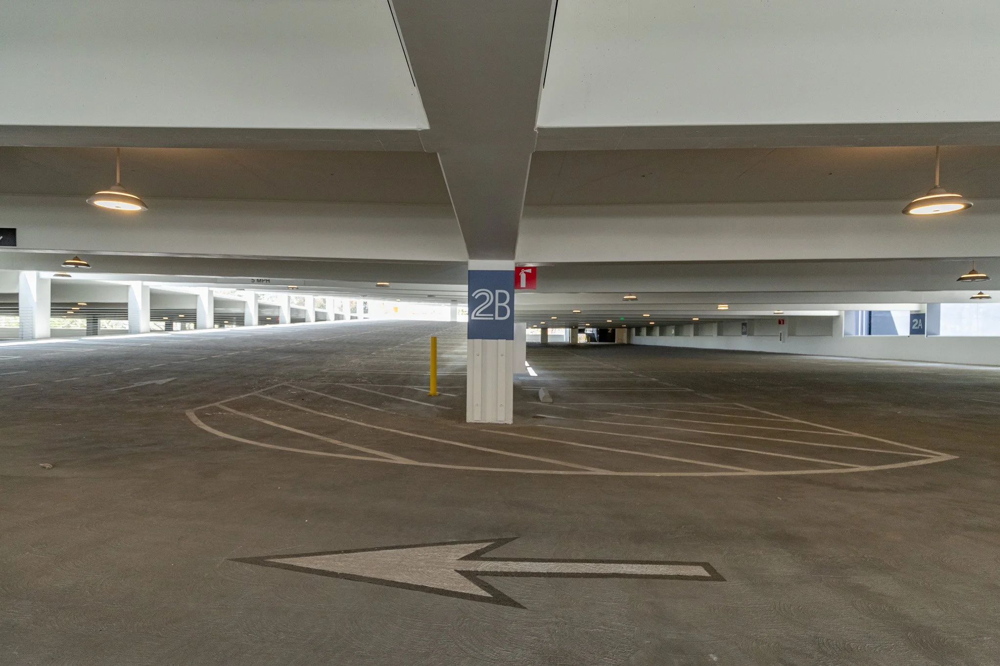 Empty multi-level parking garage with marked parking spaces, ceiling lights, and signs indicating section 2B.