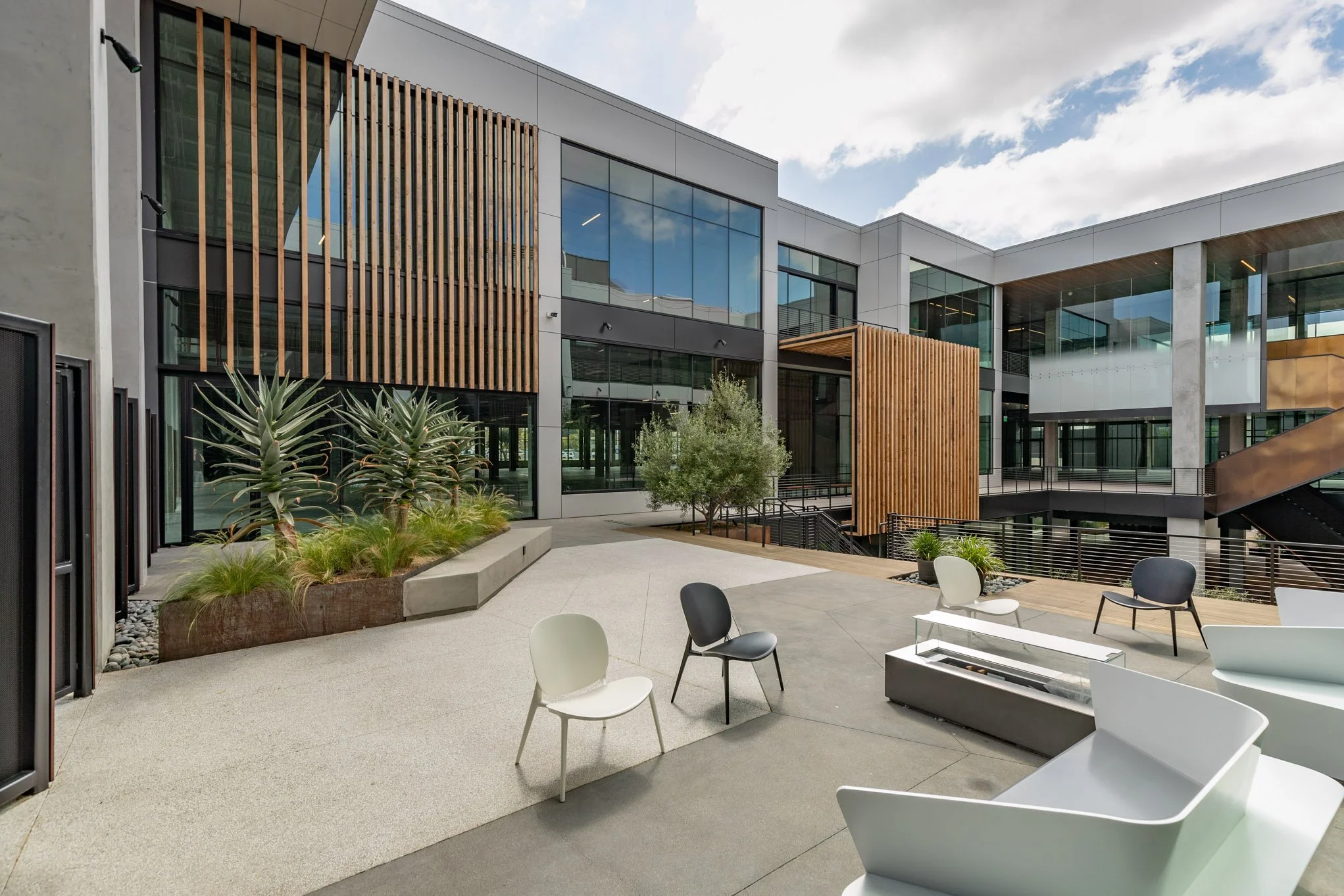 Contemporary outdoor courtyard of an office building with modern chairs, plants, and a glass facade.