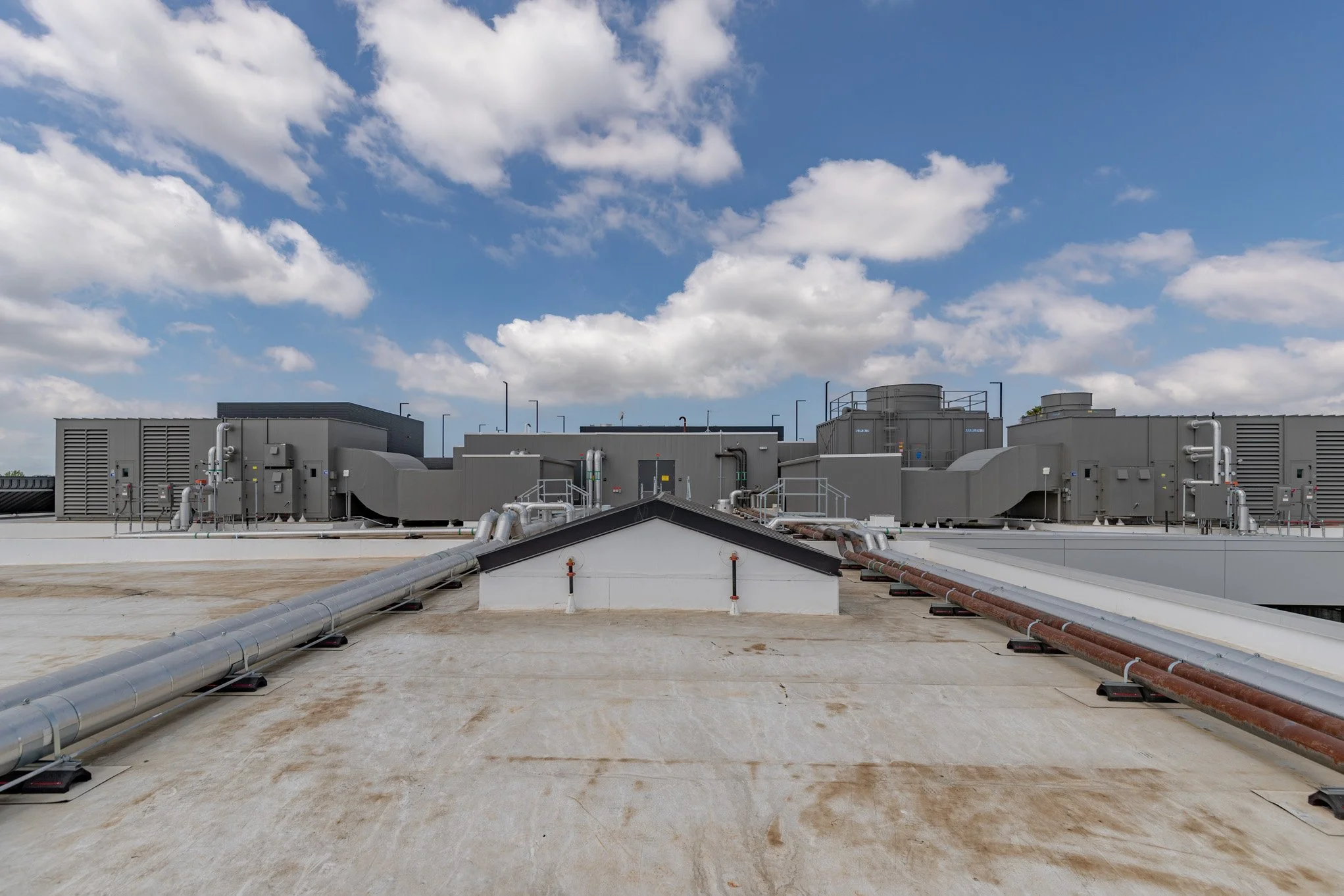 Industrial rooftop with HVAC units, ducts, and ventilation systems under a blue sky with scattered clouds.