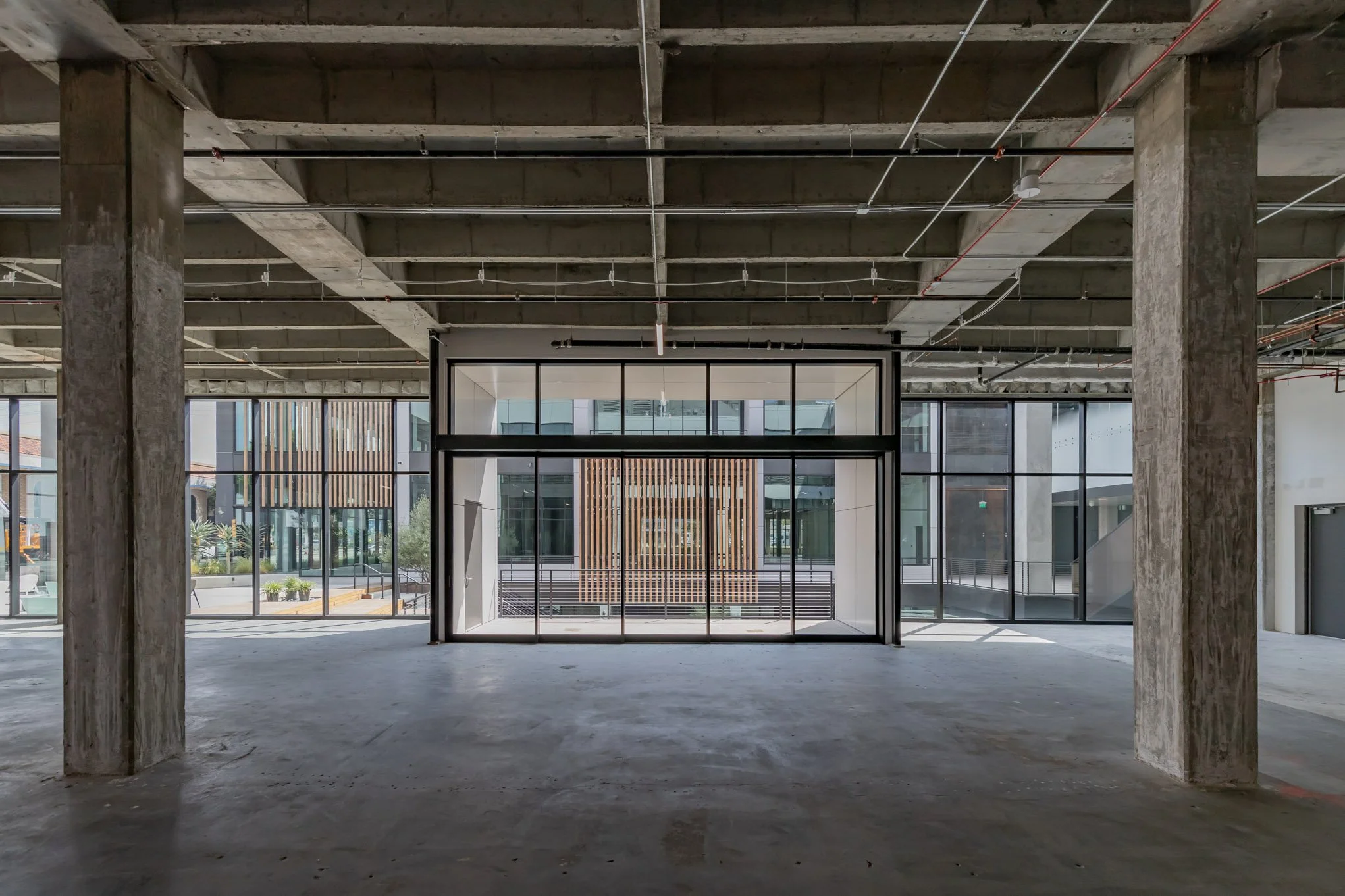 Interior of an unfinished modern building with large glass windows and exposed concrete beams and pillars.