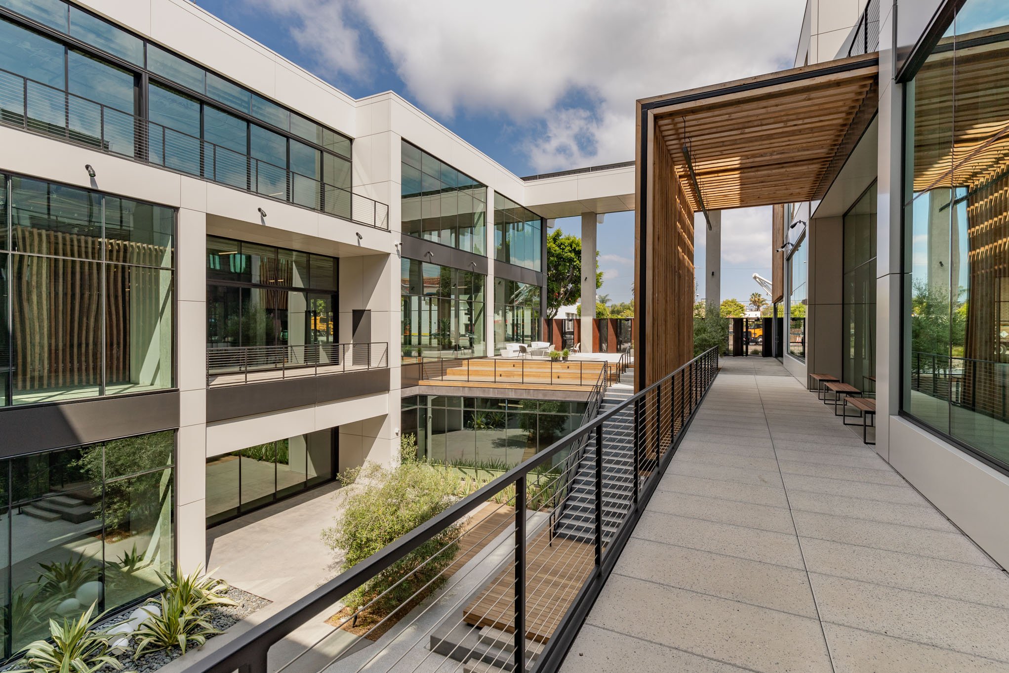 Modern multi-story office building with glass windows and an outdoor balcony walkway with seating and greenery.