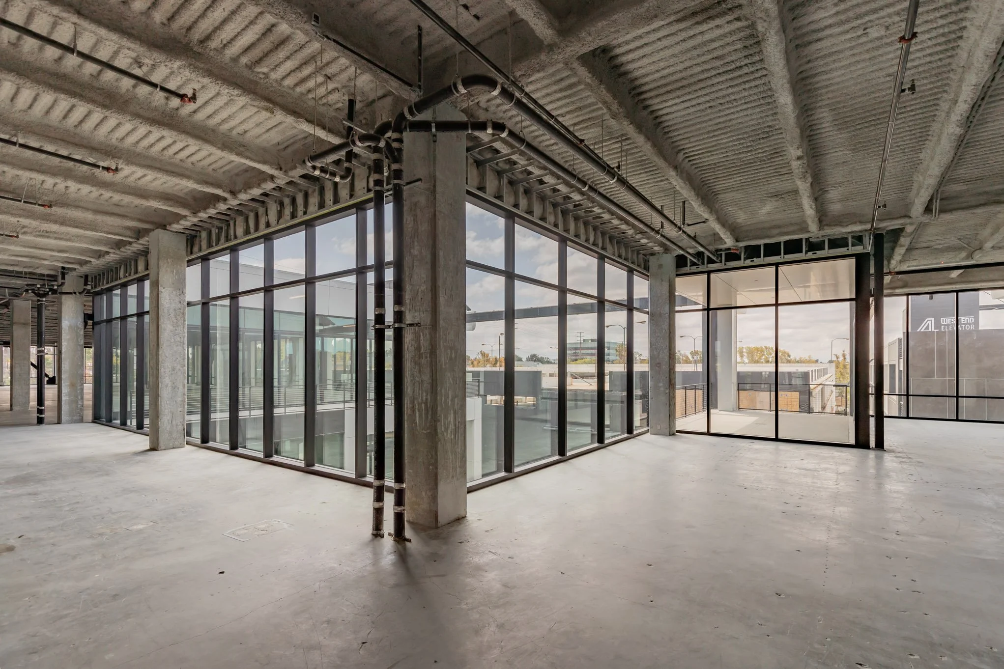 Empty unfinished commercial building with large glass windows and visible concrete columns and ceiling.