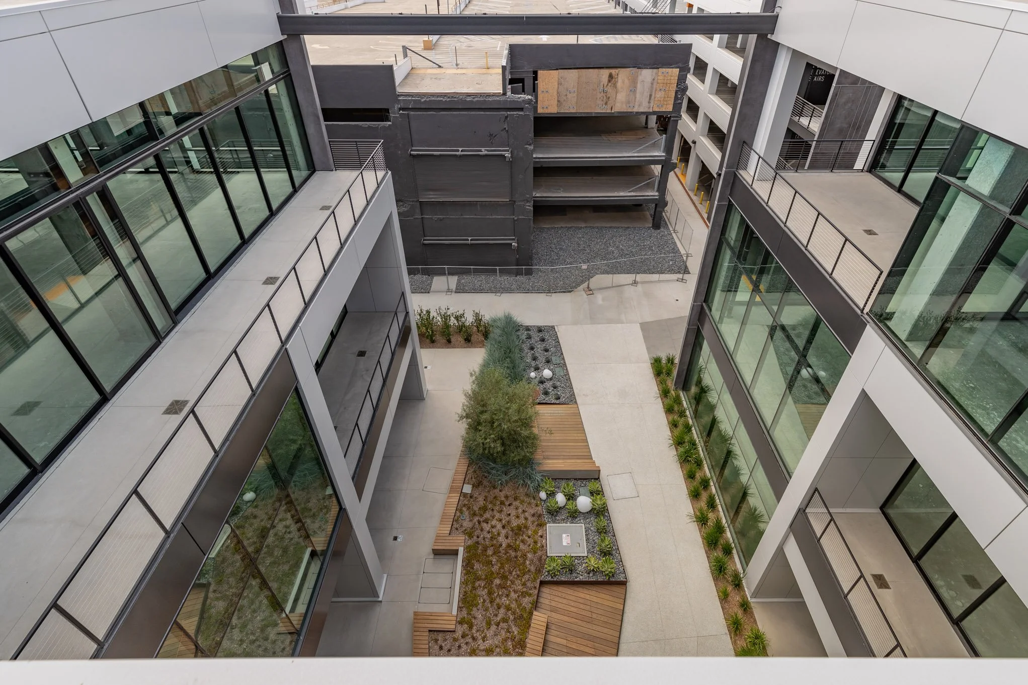 View from above of a modern urban courtyard surrounded by multi-story glass buildings with landscaped areas and walkways.