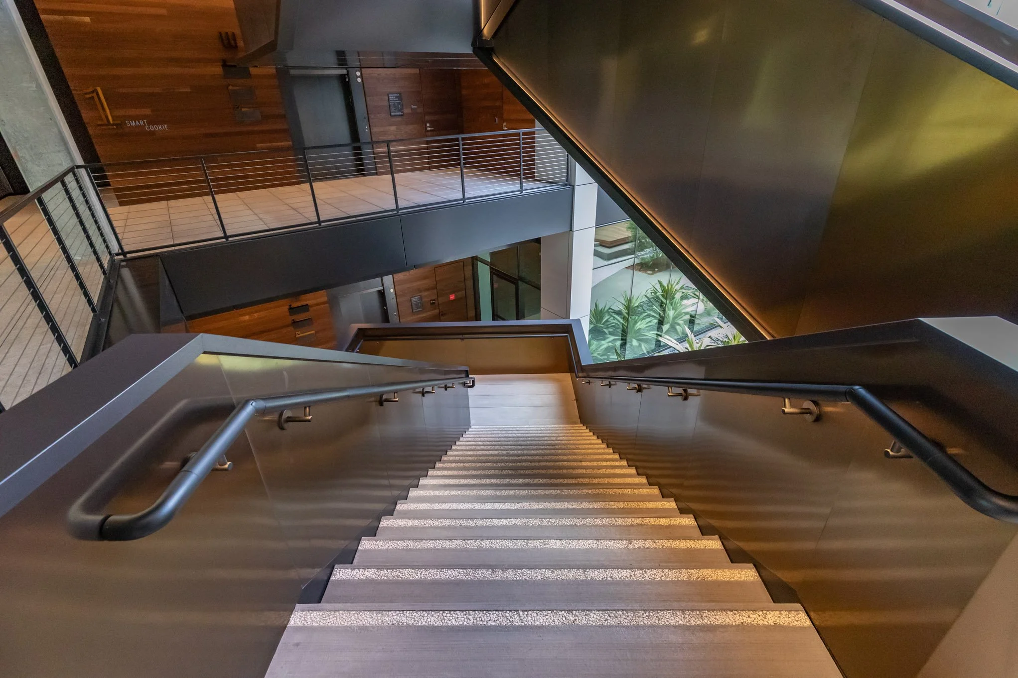 Looking down a modern staircase with metal railings in a multi-story building with wood and glass interior design.