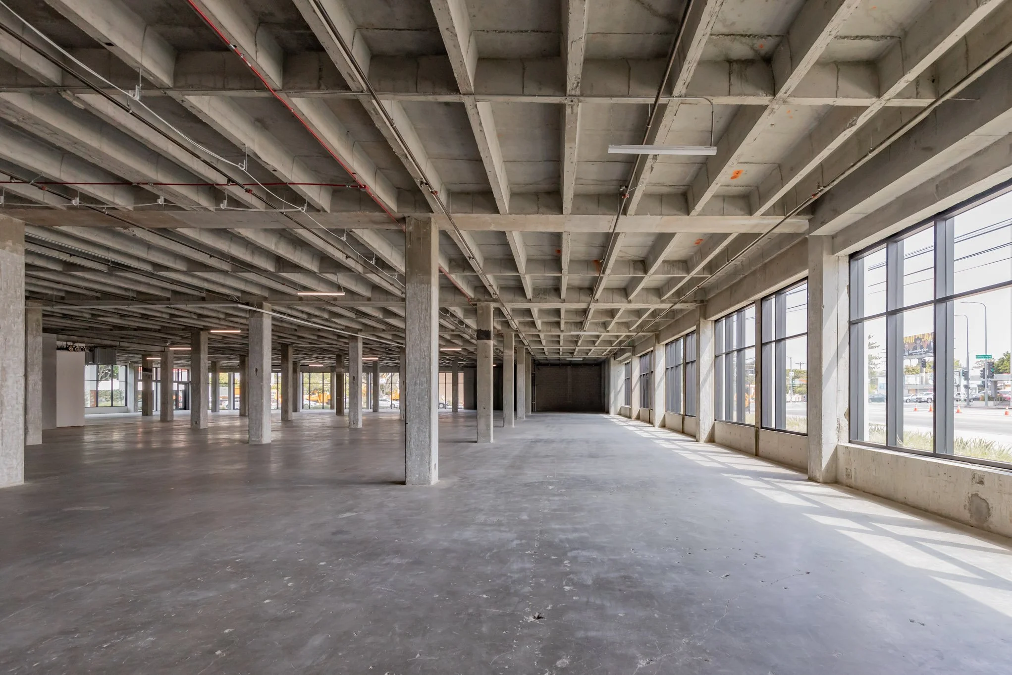 Empty commercial space with concrete floors, exposed ceiling beams, and large front windows allowing natural light.