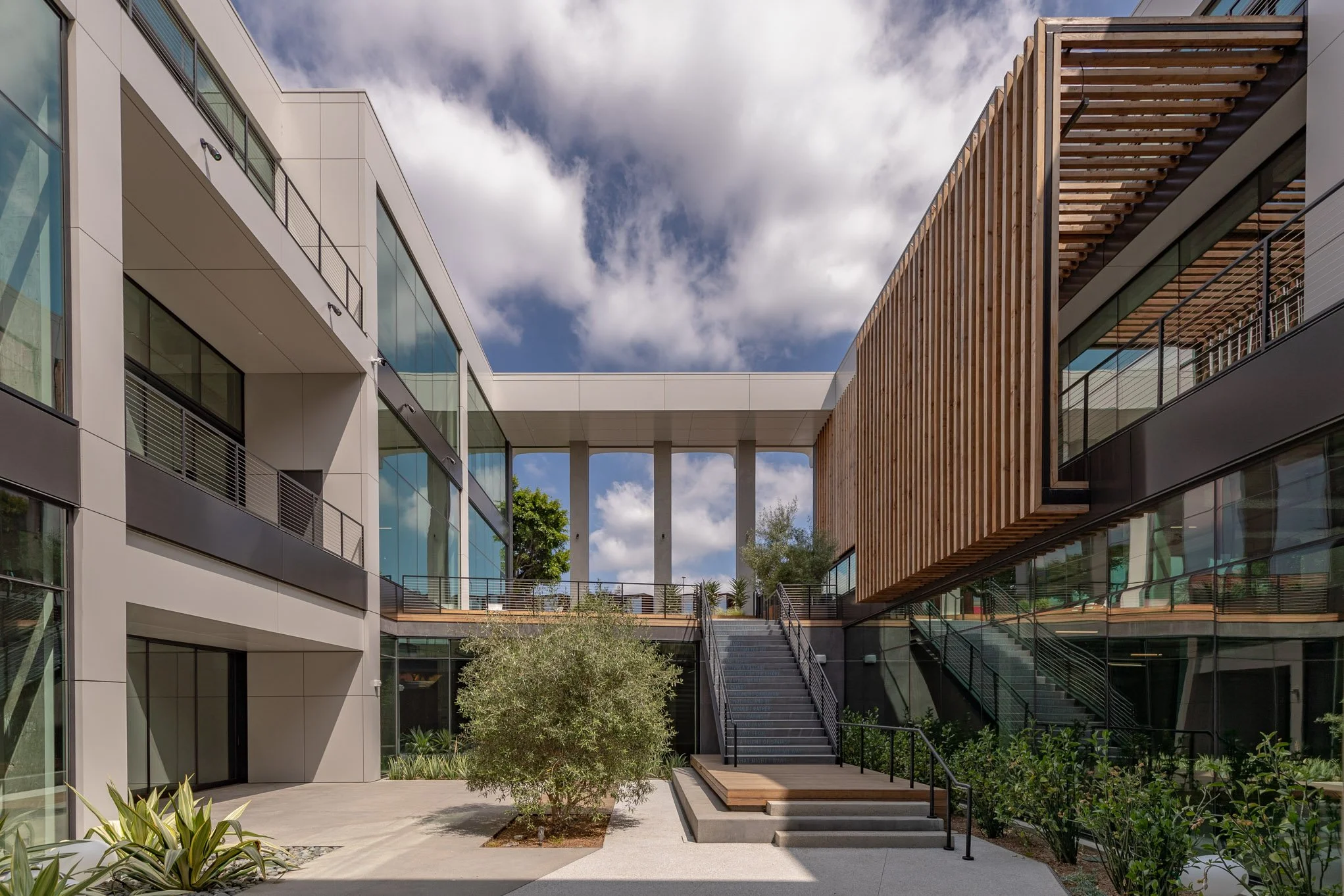 Modern apartment complex courtyard with stairs and greenery under partly cloudy sky