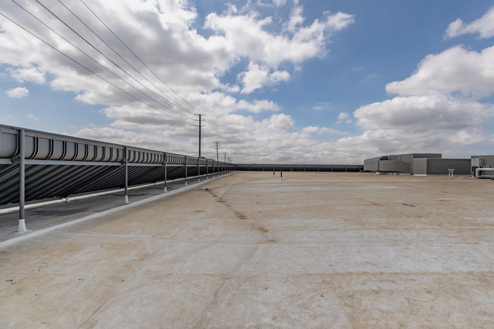 Empty rooftop with air conditioning units, metal railing, electrical lines, and a cloudy sky.