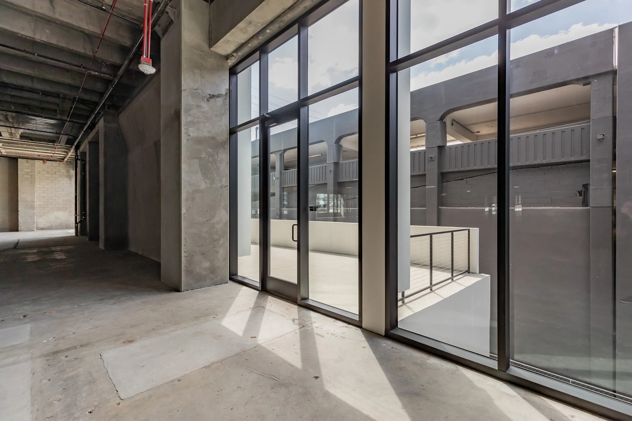 Empty industrial-style interior with large floor-to-ceiling glass windows and concrete walls.