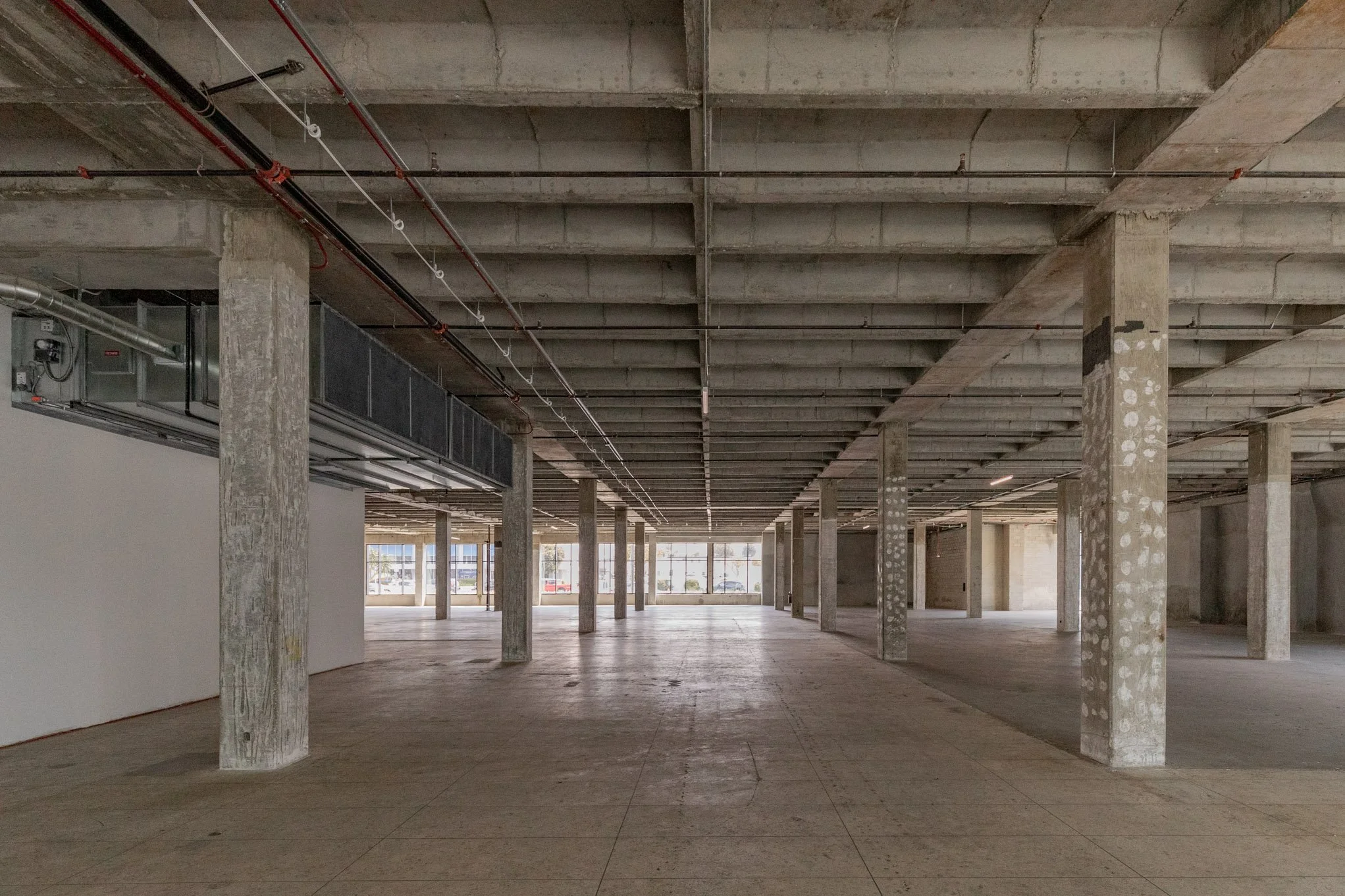 Empty commercial space under construction with concrete columns, exposed ceiling, and large front windows.