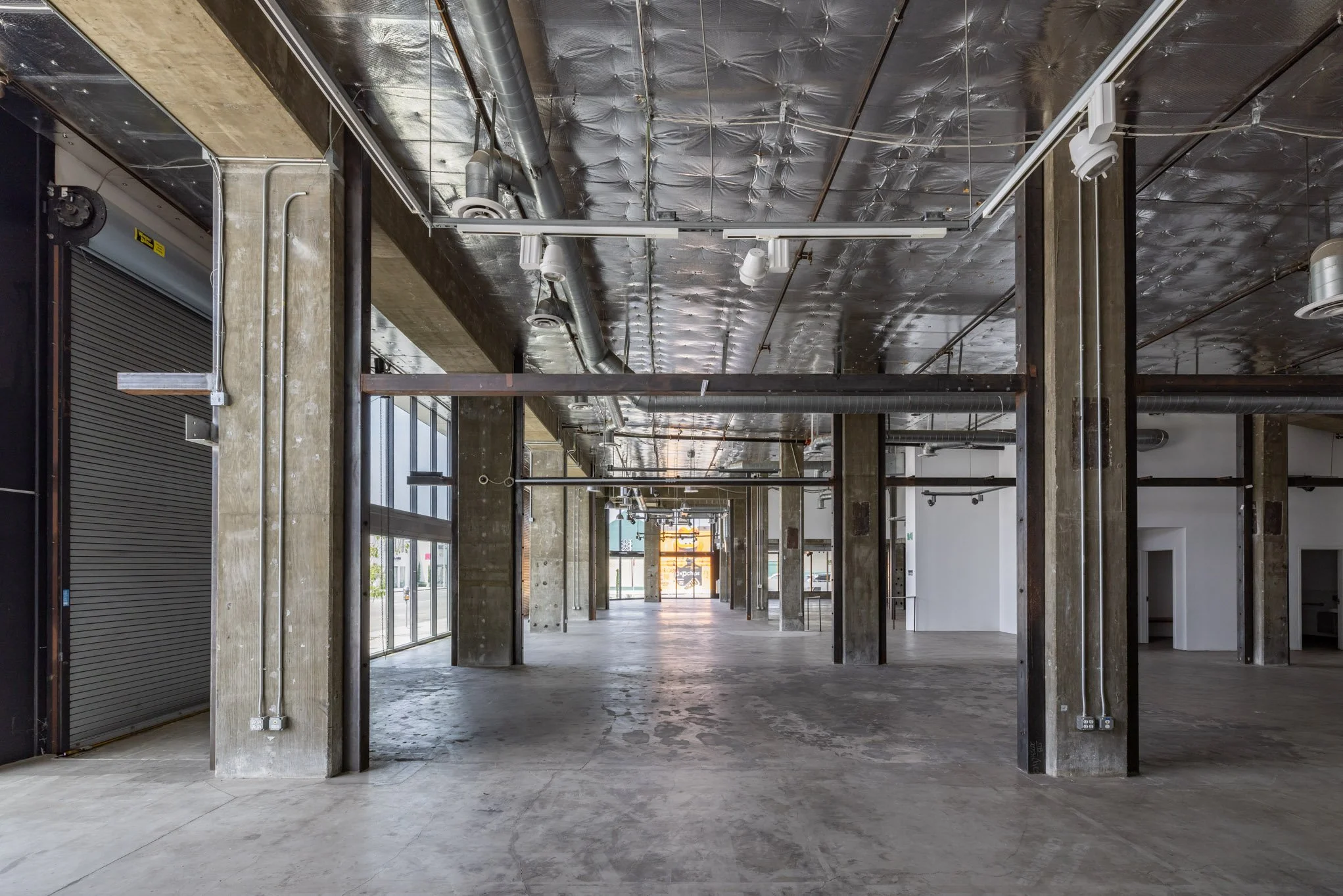 Empty industrial-style commercial or retail space with exposed concrete columns, ductwork, and a polished concrete floor.