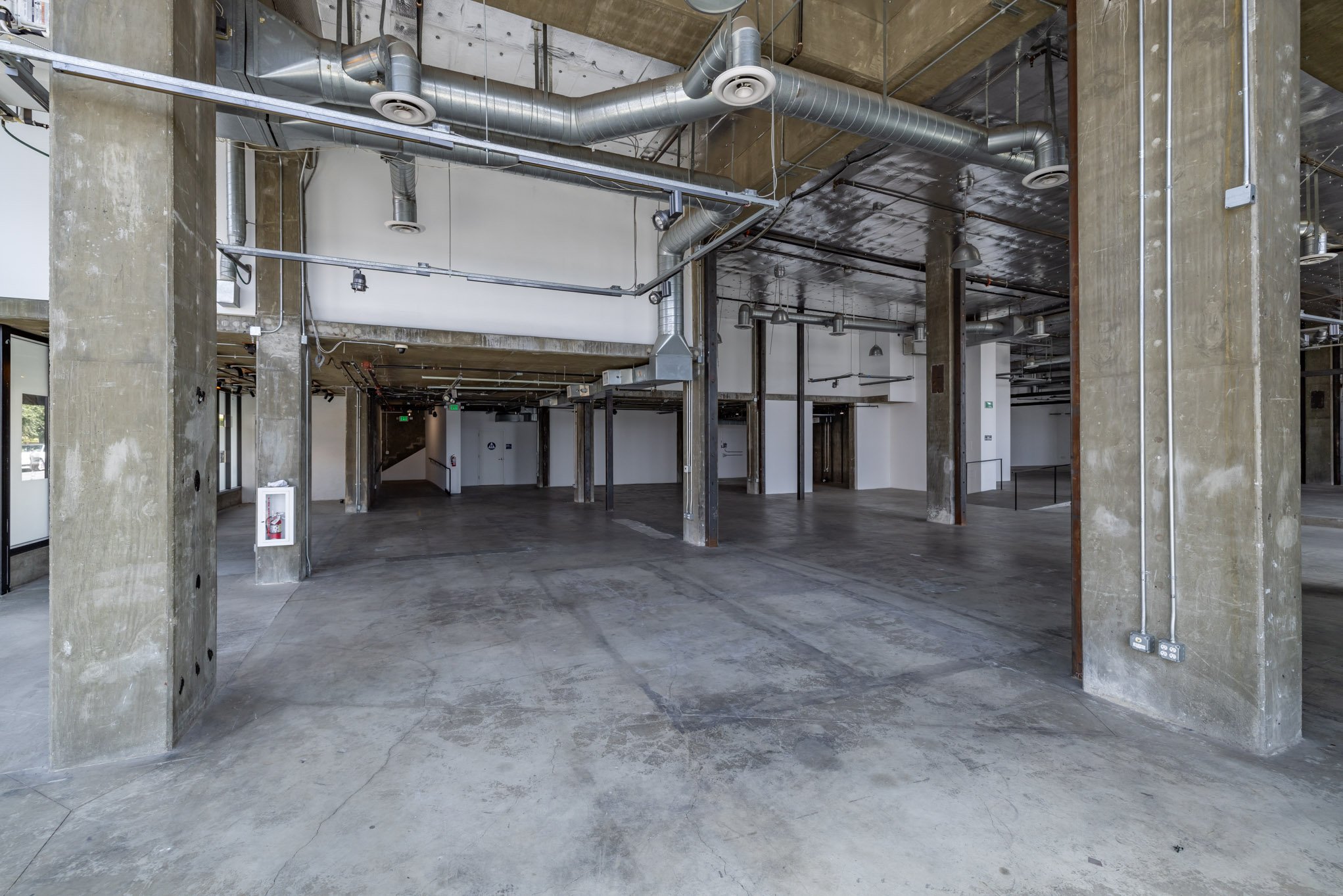 Empty industrial warehouse with concrete floors, exposed ductwork, and concrete support columns.