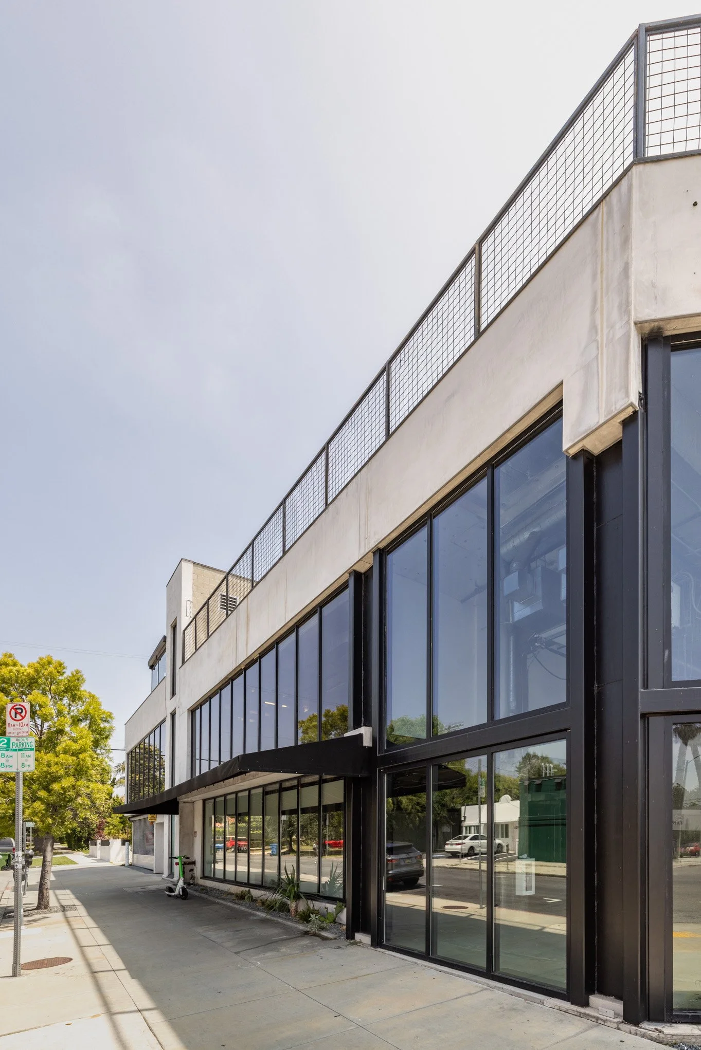 Modern building with large glass windows on sidewalk, trees and parked cars visible outside.