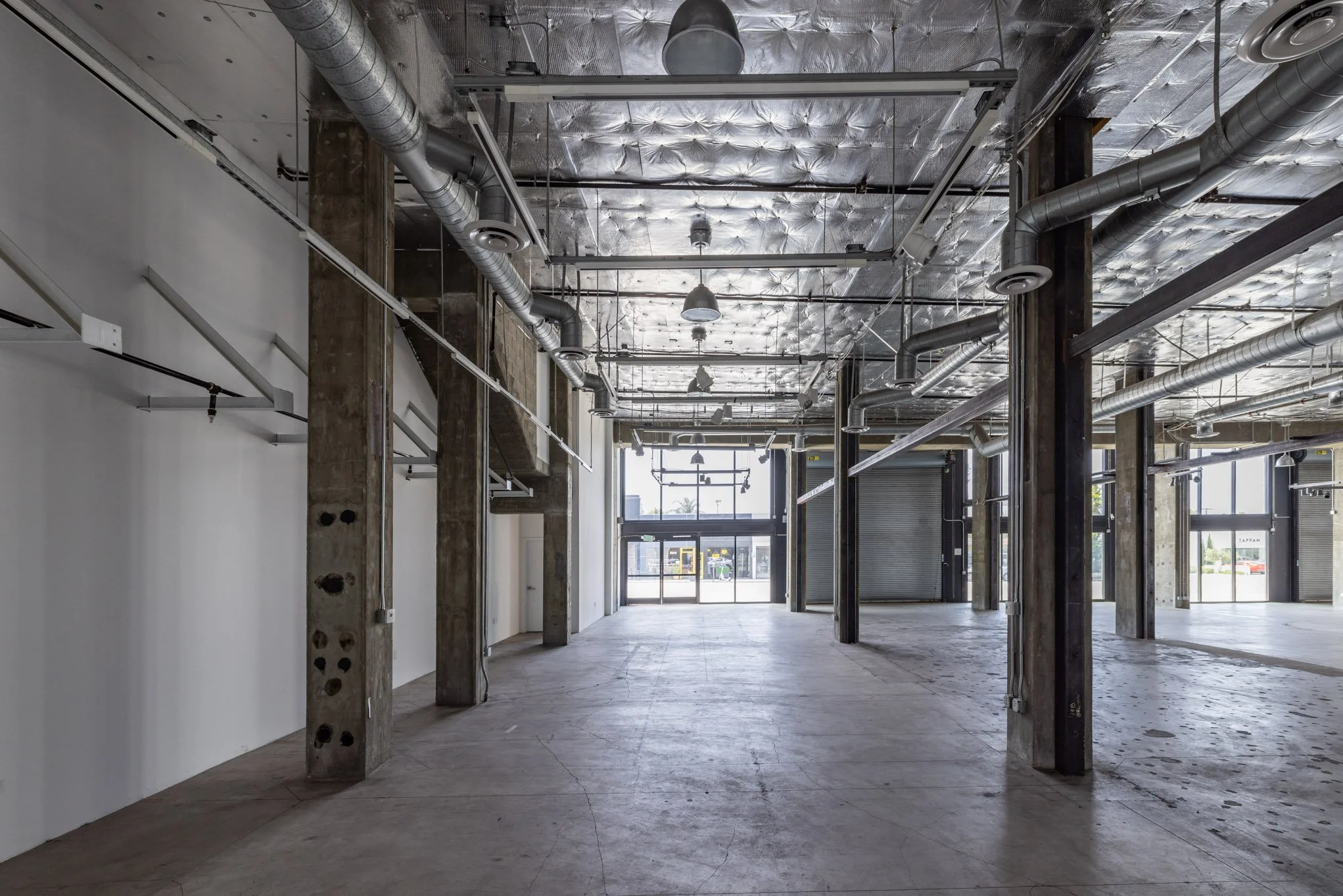 Empty commercial space with unfinished ceiling, exposed ductwork, and large front windows.