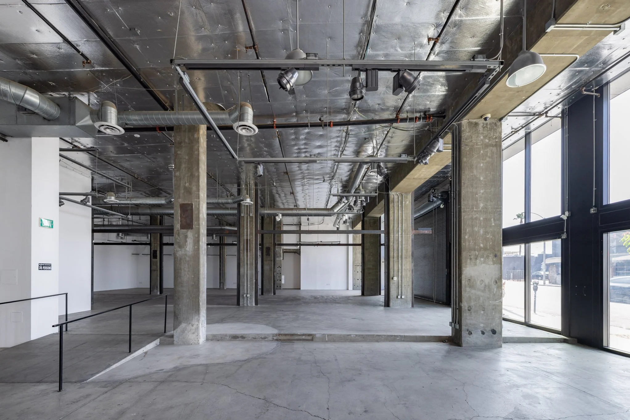 Empty commercial space with exposed ceiling, concrete support columns, large glass windows, and polished concrete floors.