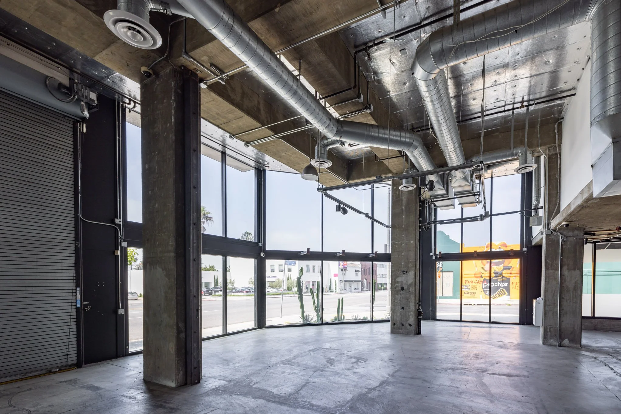 Empty commercial space with large glass windows, visible ductwork and concrete columns.