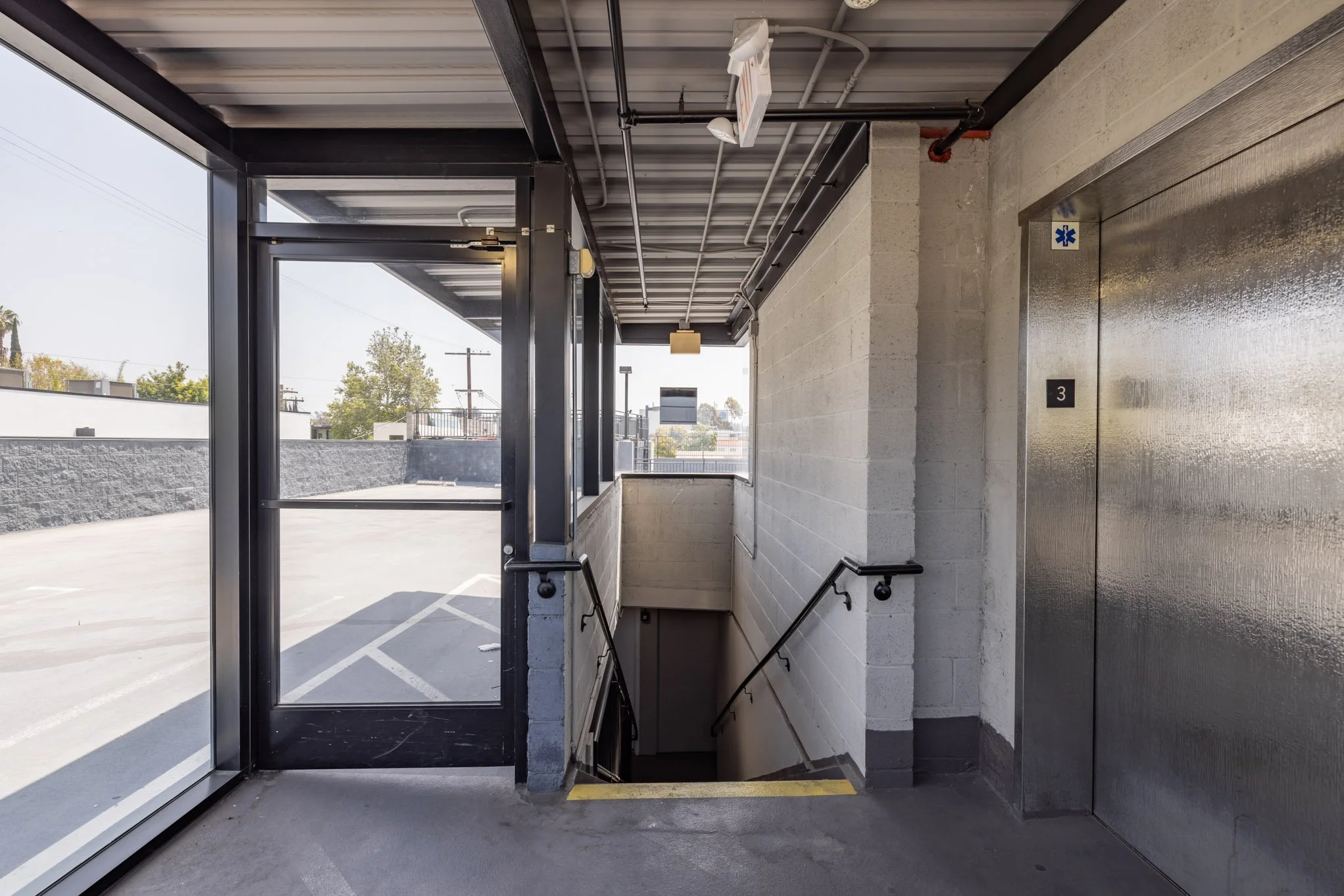 Entrance to an underground parking garage with stairs leading down, a glass door, and an elevator to the right.