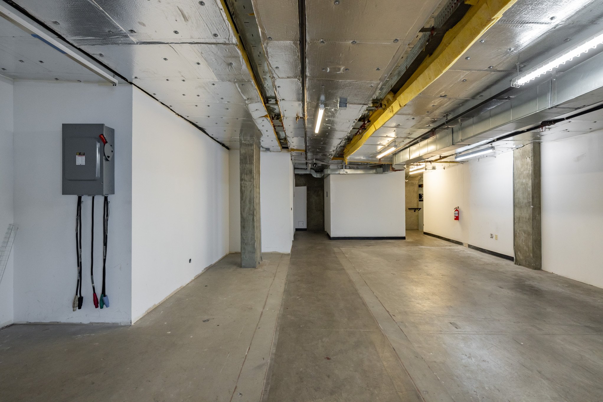 Empty indoor parking garage with concrete floors, white walls, exposed ceiling with ductwork, and emergency fire equipment.