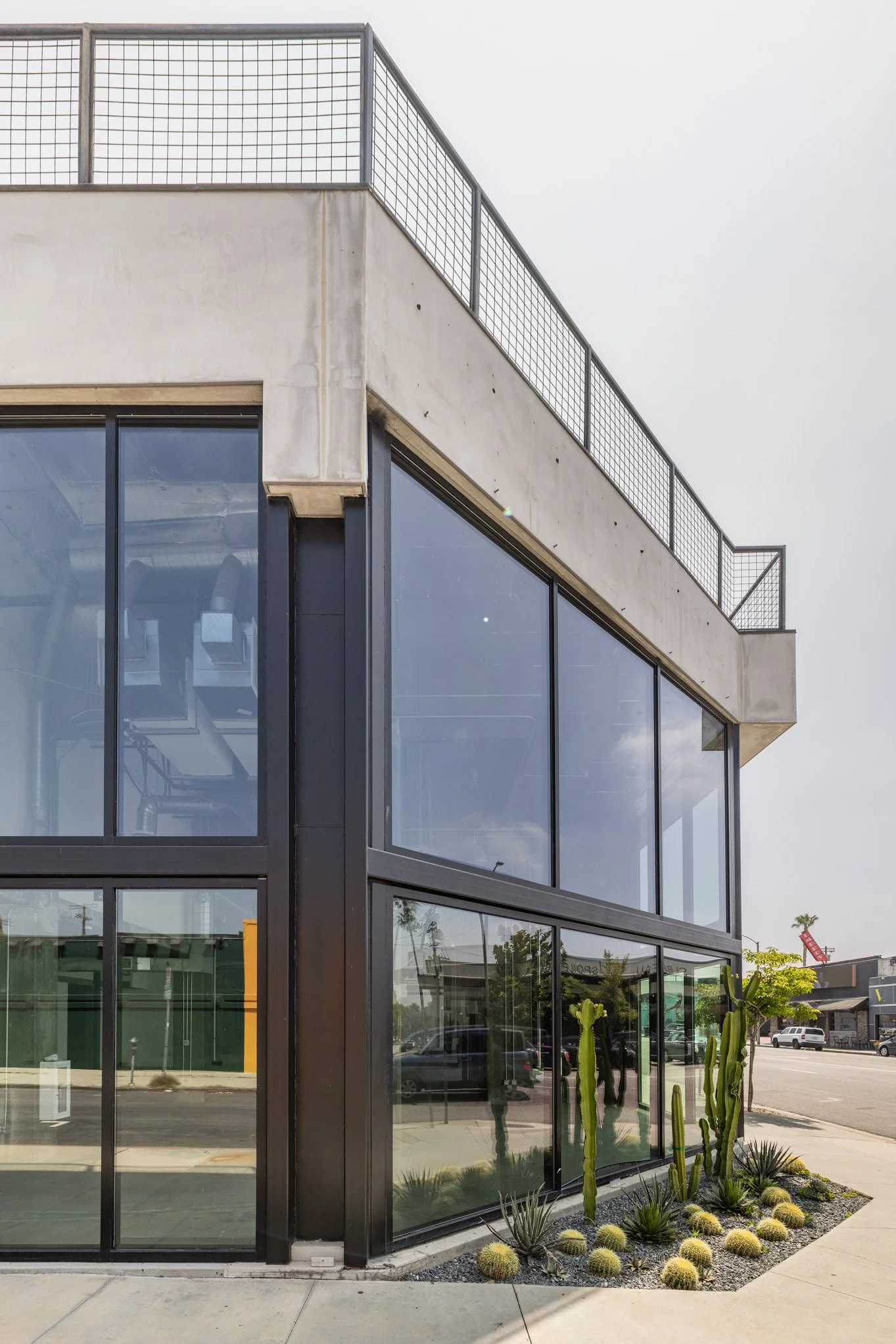 Modern building with large glass windows and a rooftop railing, with desert cacti and succulents in front.