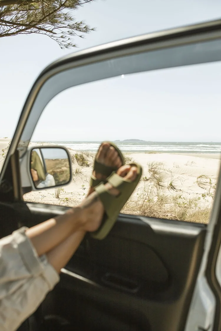 Feet up on a car dashboard looking out to a sandy beach