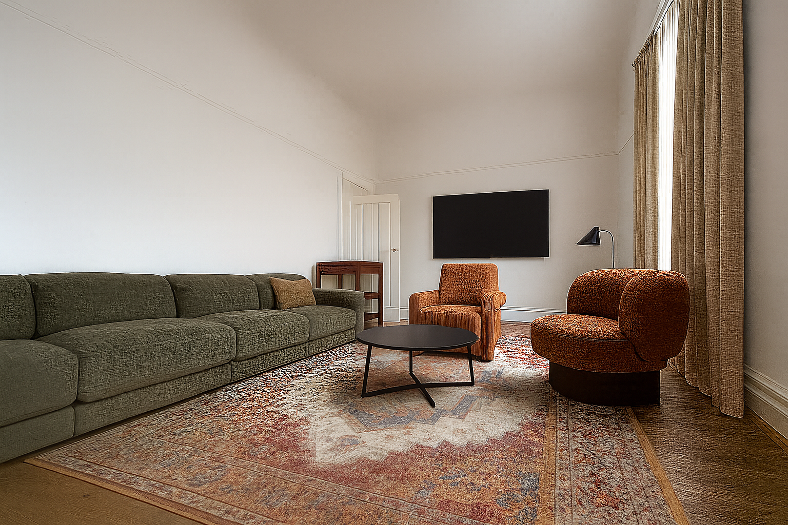 A living room with a long green sofa, two orange armchairs, a black coffee table, a large wall-mounted TV, a floor lamp, a small wooden side table, patterned curtains, and a colorful area rug.