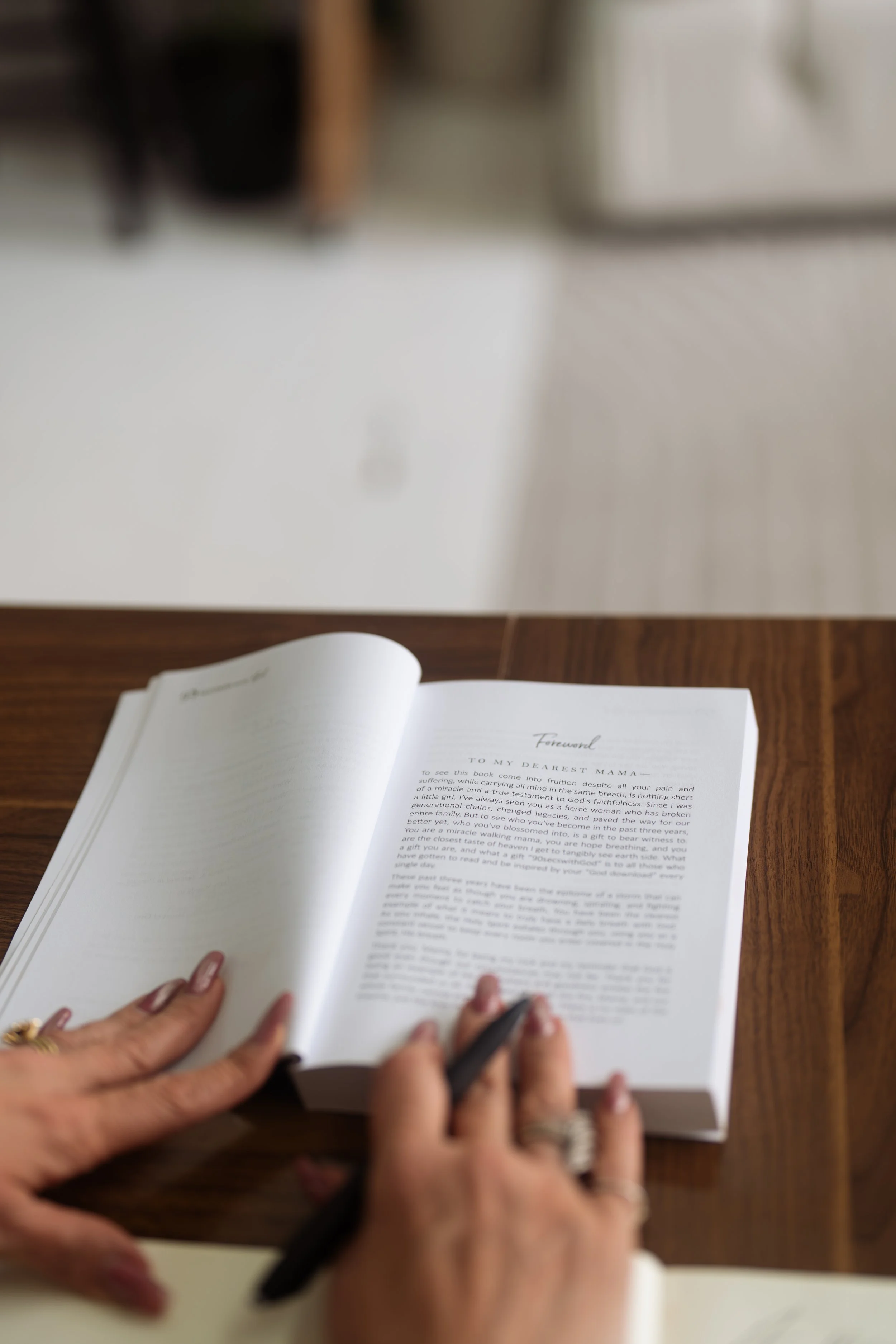 Open book on a wooden table with a person writing or taking notes, blurred background.