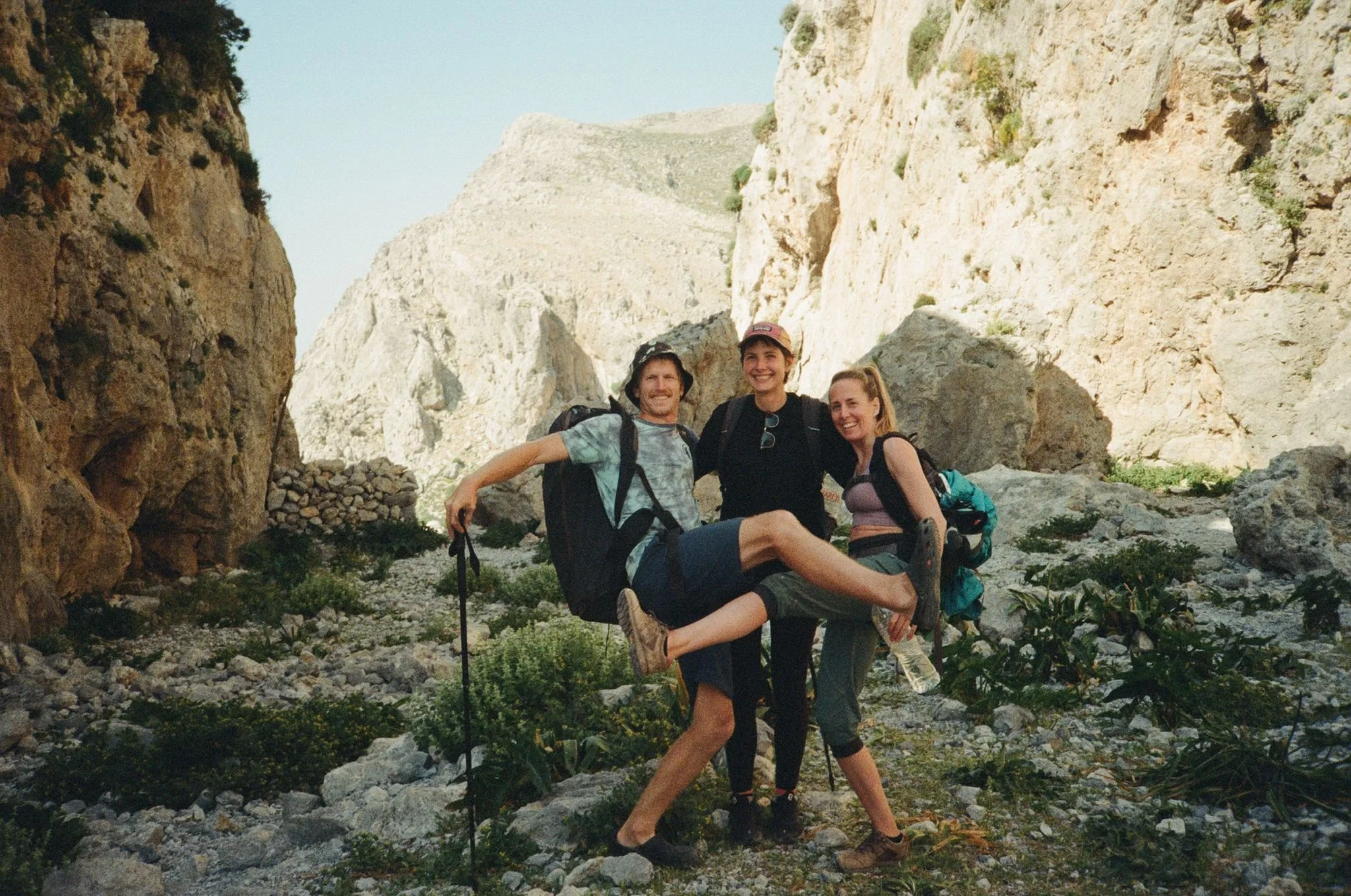 Trois personnes souriantes en randonnée dans un canyon rocheux, portant des sacs à dos et des équipements de marche.